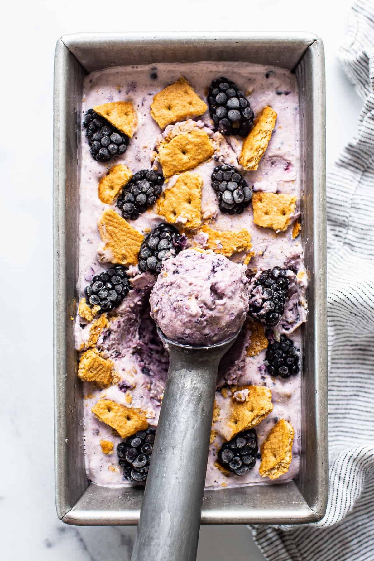 blackberry cheesecake cottage cheese ice cream in a bread pan topped with fresh blackberries and graham cracker crumbs.