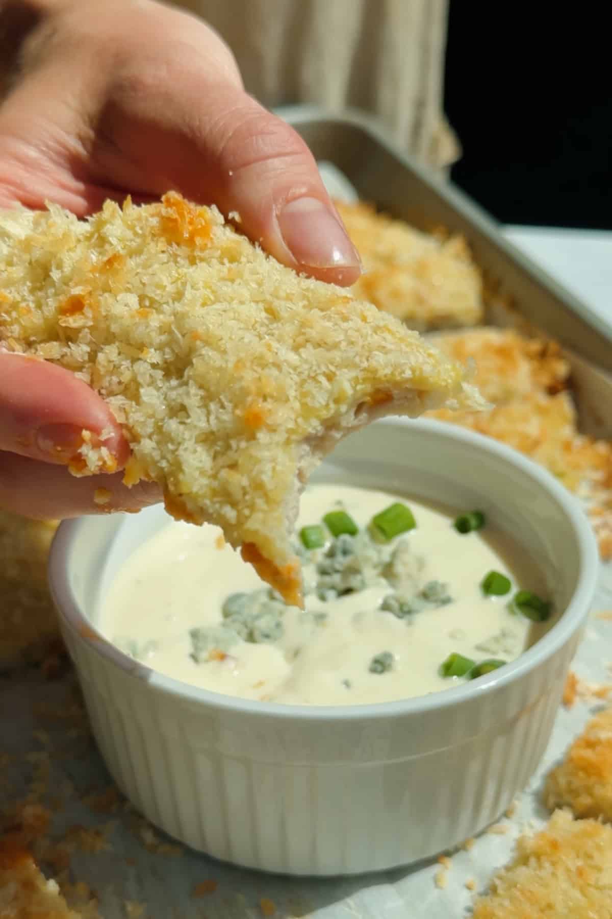 Dipping a crispy chicken protein bar into blue cheese dressing topped with crumbled cheese and green onions
