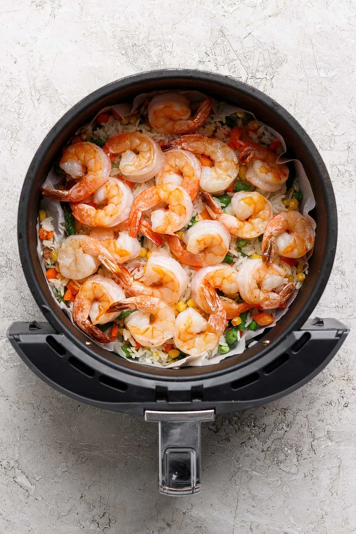 Raw shrimp and mixed vegetables arranged in a single layer inside an air fryer basket, ready to be cooked.