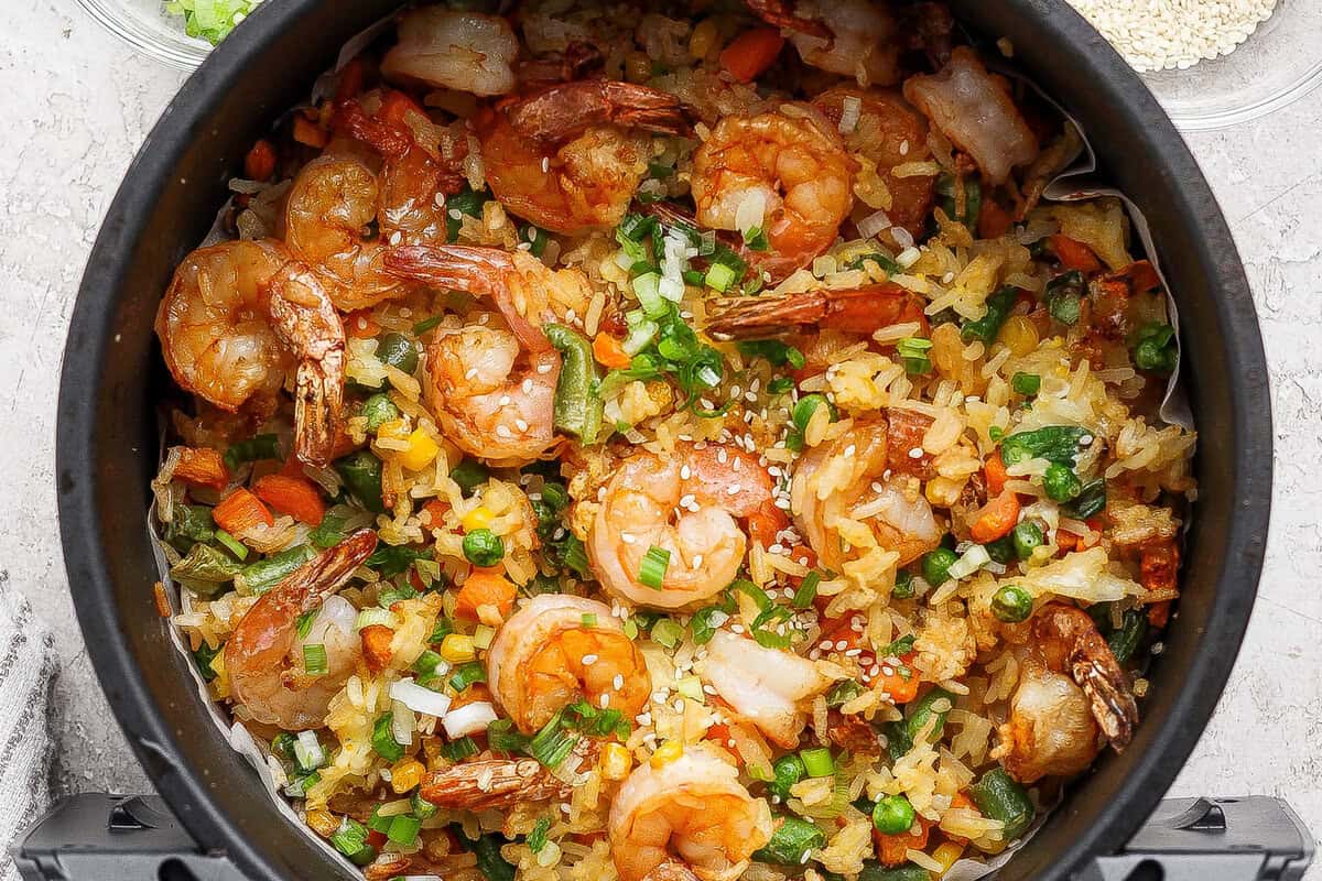 A close-up of cooked shrimp fried rice with mixed vegetables, garnished with chopped green onions, served in a black bowl.