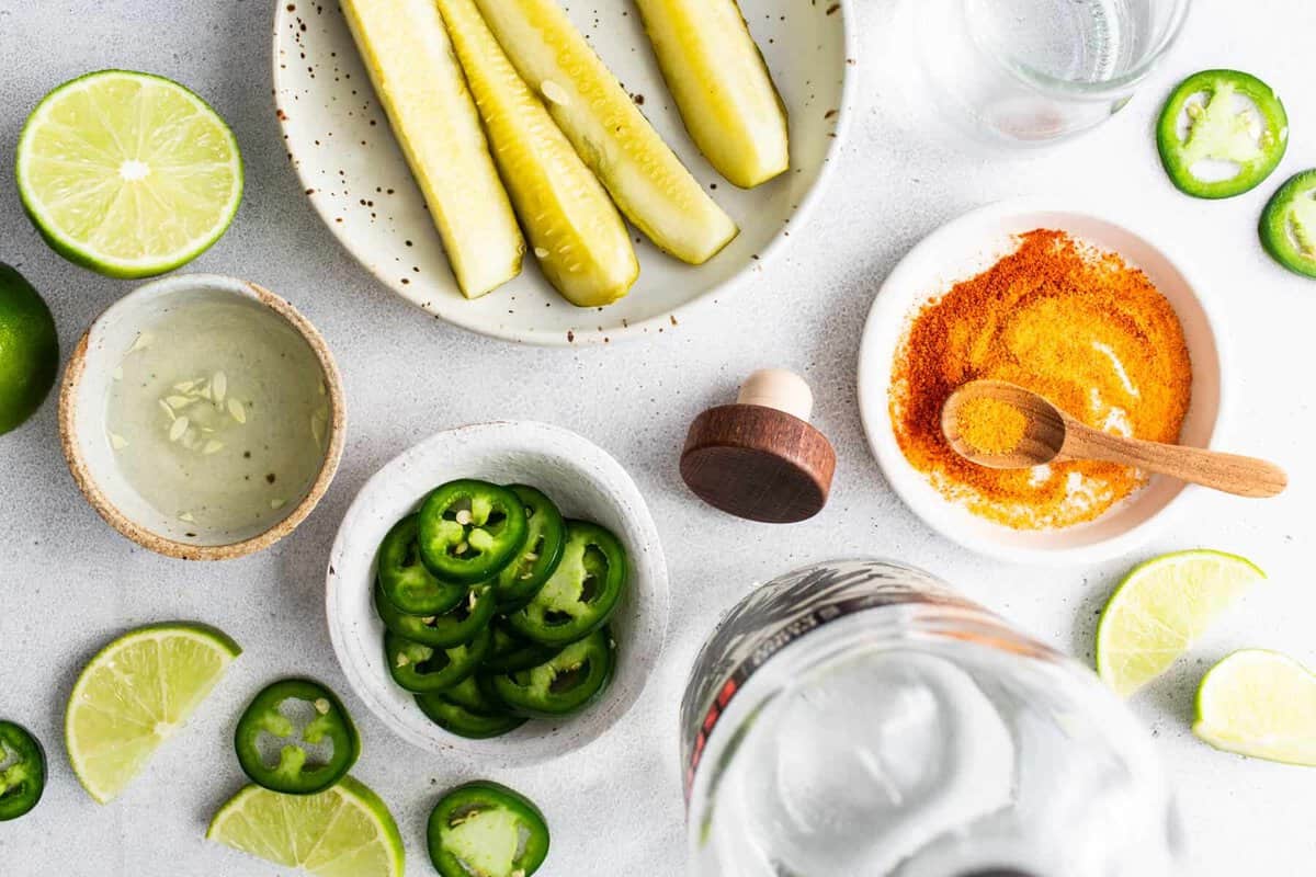 Spicy pickle margarita ingredients including jalape&ntilde;os, limes, pickle juice, and tequila.
