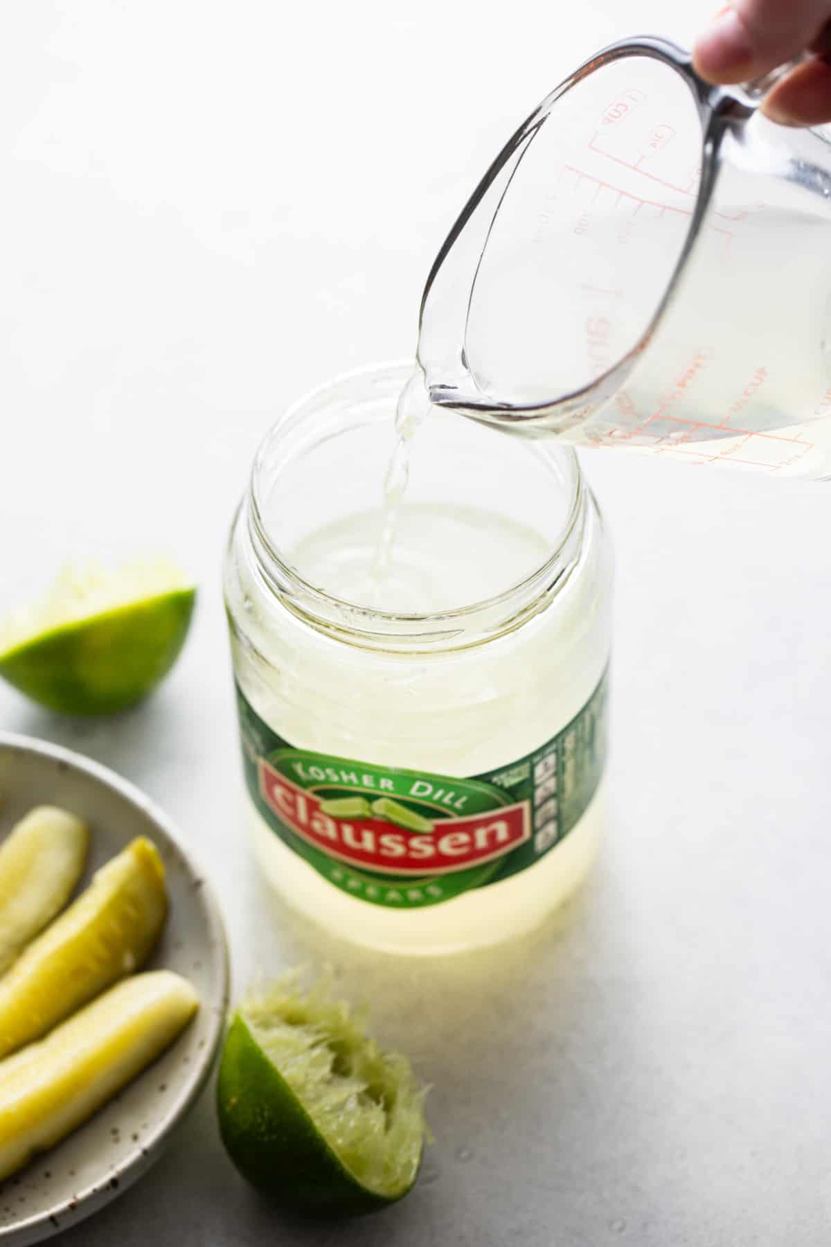 Pouring pickle juice into a cocktail shaker for a spicy pickle margarita.