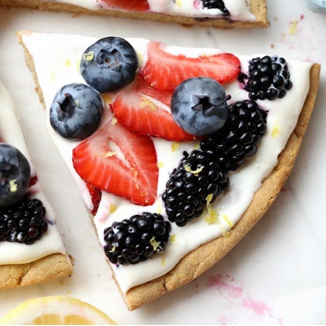 A slice of pizza with berries and lemon on it.