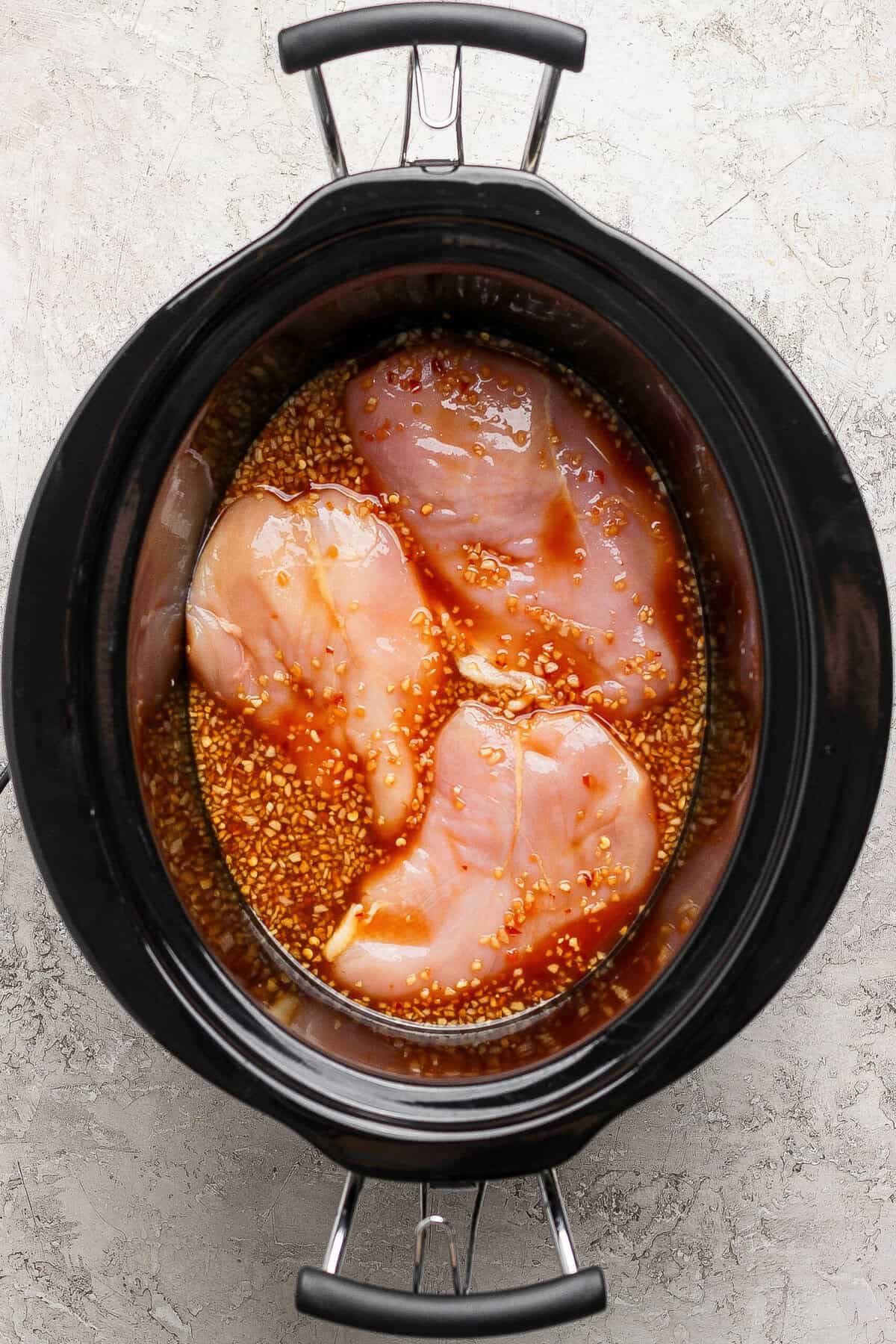 Raw chicken breasts in a crockpot with honey garlic sauce ready to cook