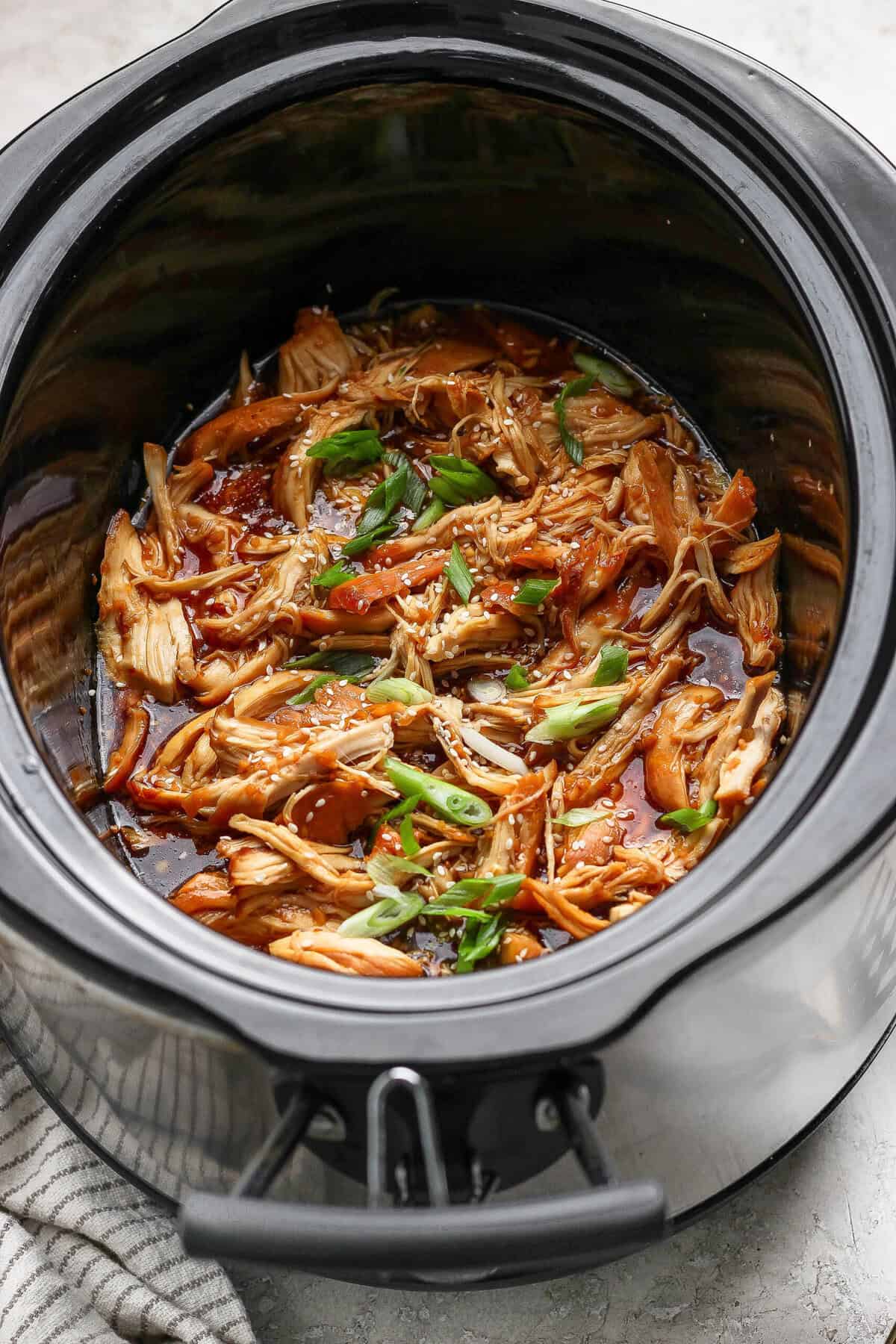 Closeup of shredded honey garlic chicken in a crockpot with sesame seeds and green onions