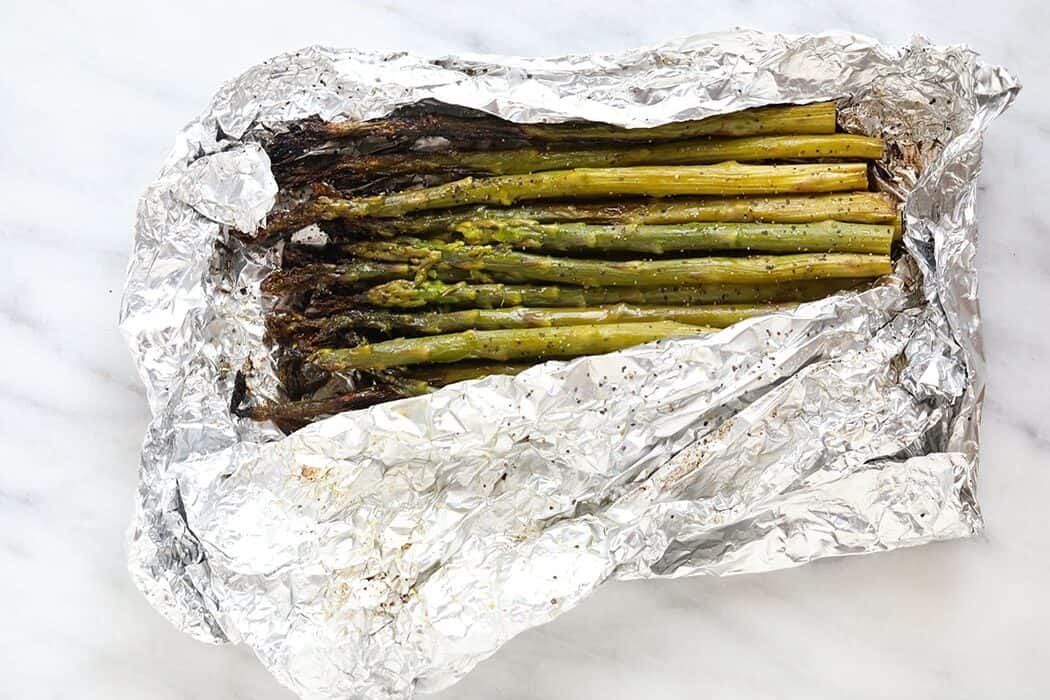grilled asparagus in foil on a white plate with lemon wedges