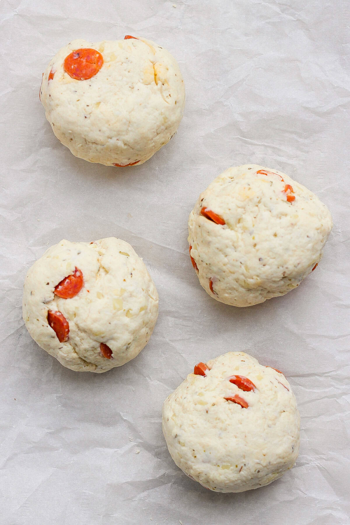 Four pizza protein bagel dough balls with pepperoni on parchment paper