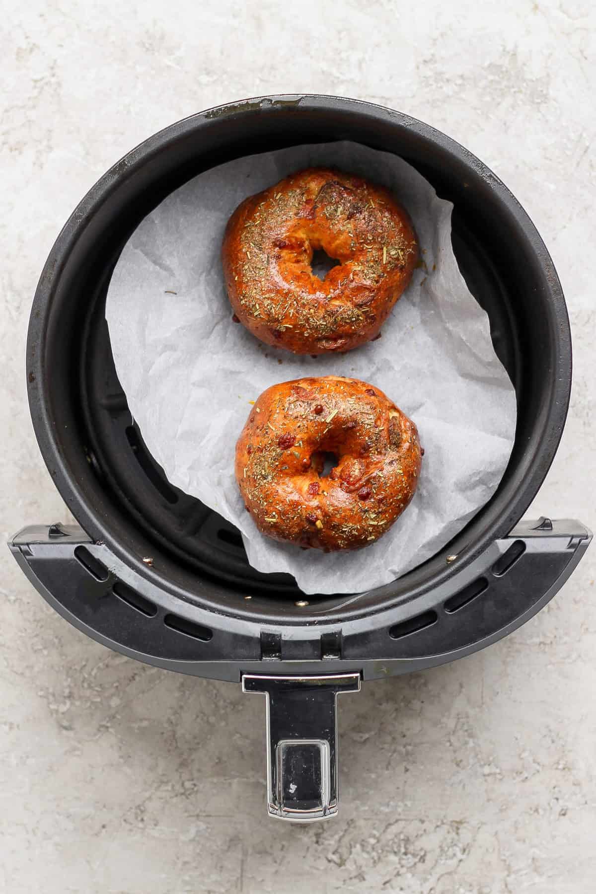 Two baked pizza protein bagels with Italian seasoning in an air fryer basket