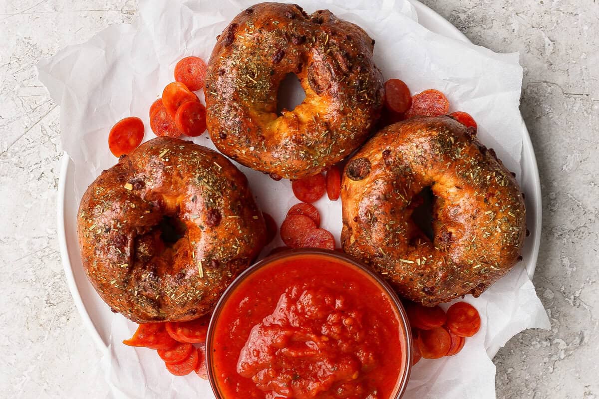 Three pizza protein bagels on parchment paper served with marinara sauce and pepperoni