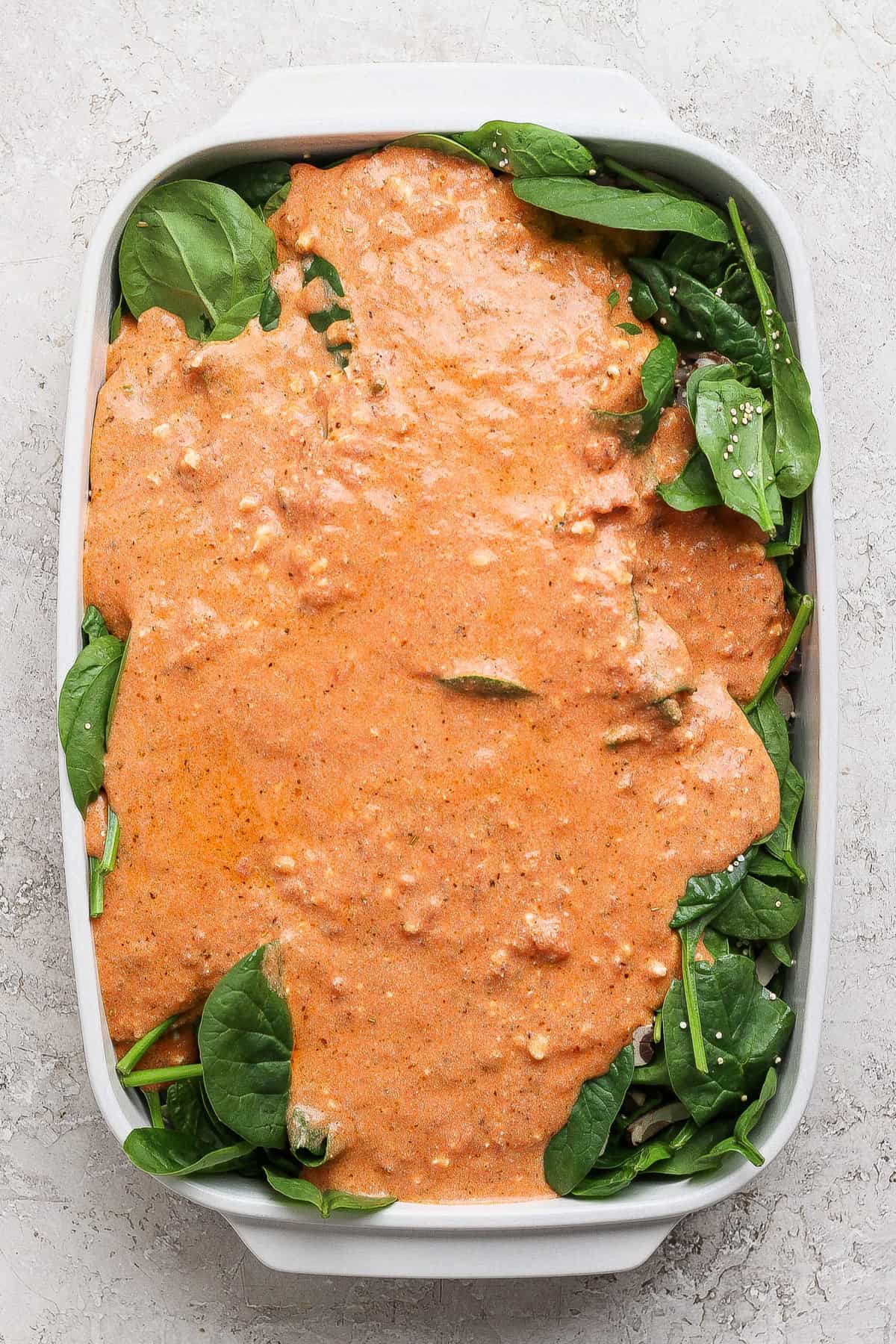 Layering cottage cheese sauce over fresh spinach in a baking dish