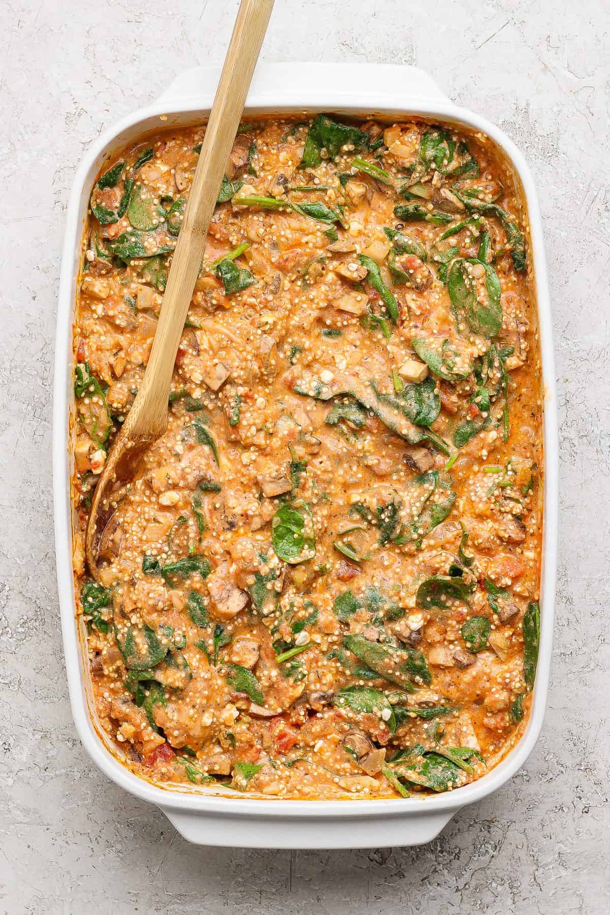 Stirring quinoa and spinach filling with a wooden spoon in a baking dish