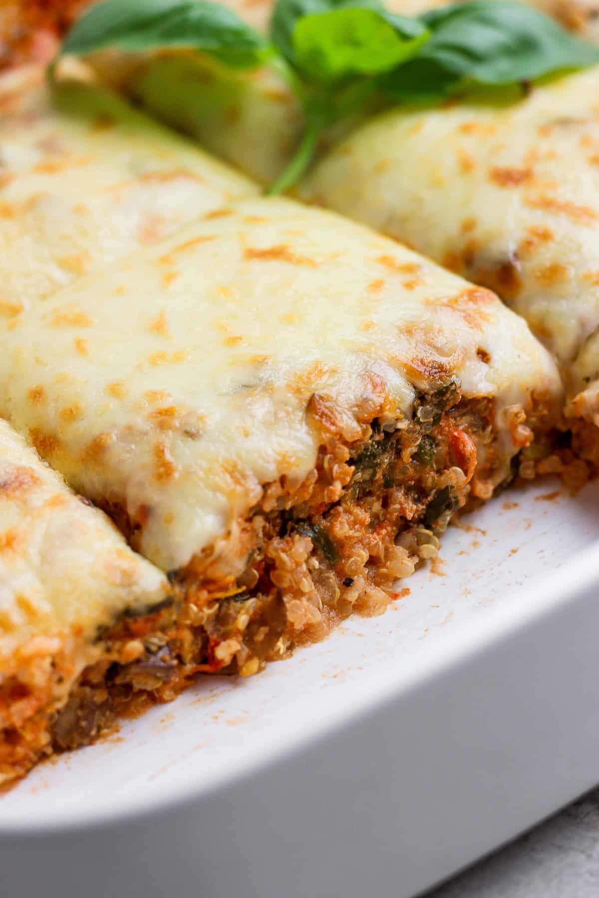 Close-up of spinach quinoa lasagna casserole slices in a white baking dish topped with melted cheese and basil