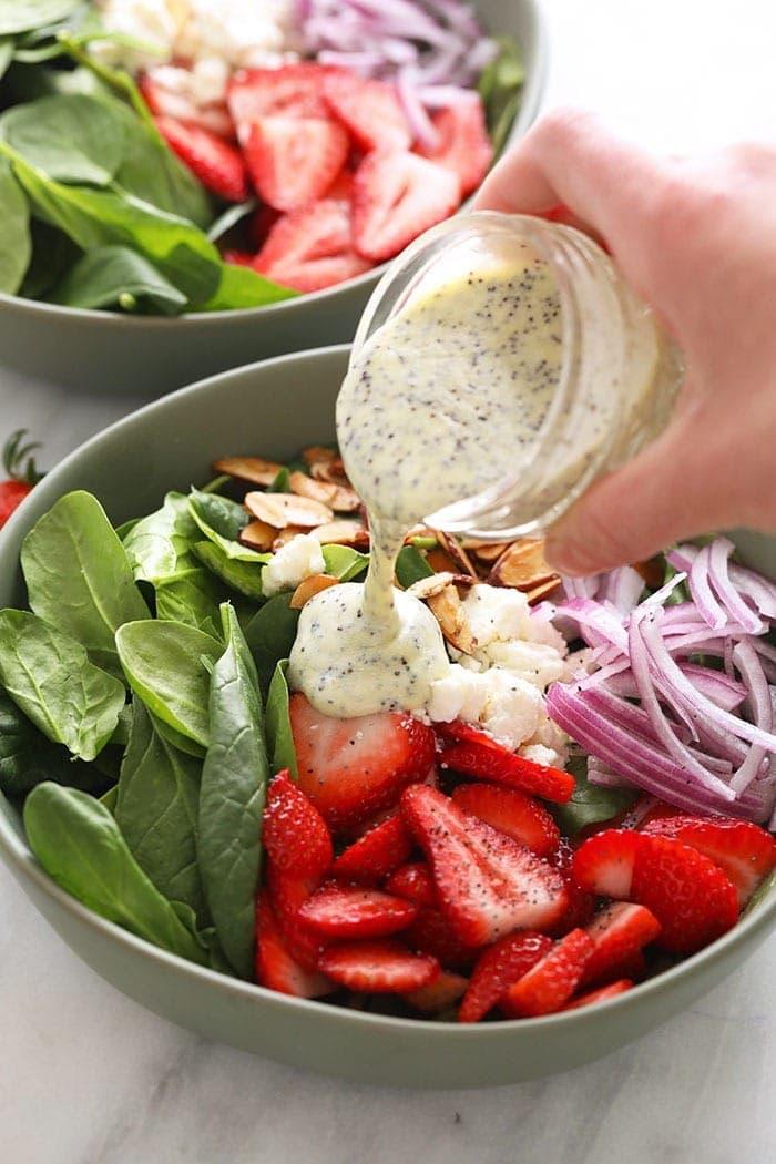 Drizzle homemade poppyseed dressing over this beautiful strawberry spinach salad Pouring poppy seed dressing over a strawberry spinach salad.