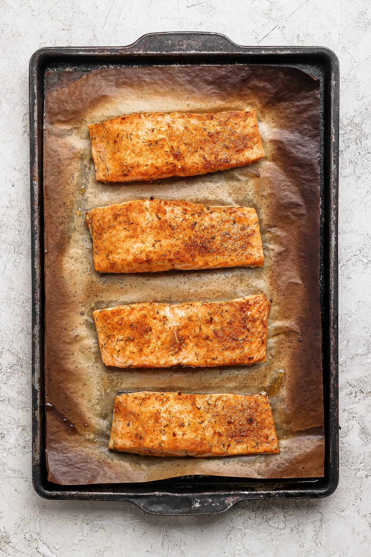 Four golden broiled salmon fillets on a parchment-lined baking sheet fresh from the oven.