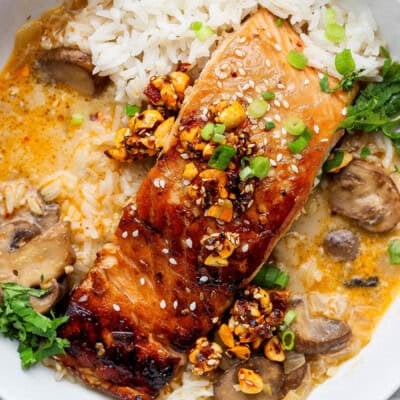 Grilled salmon topped with chopped nuts and green onions, served with white rice, mushrooms, fresh herbs, and a creamy sauce.
