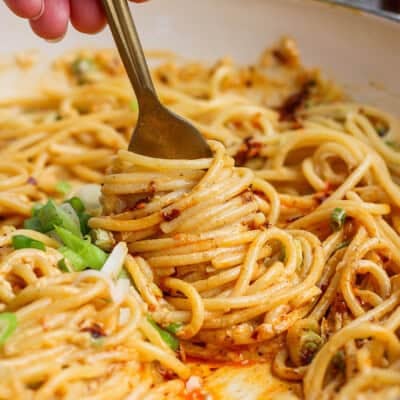 A close-up of a fork twirling spaghetti noodles coated in a creamy orange sauce, garnished with sliced green onions.