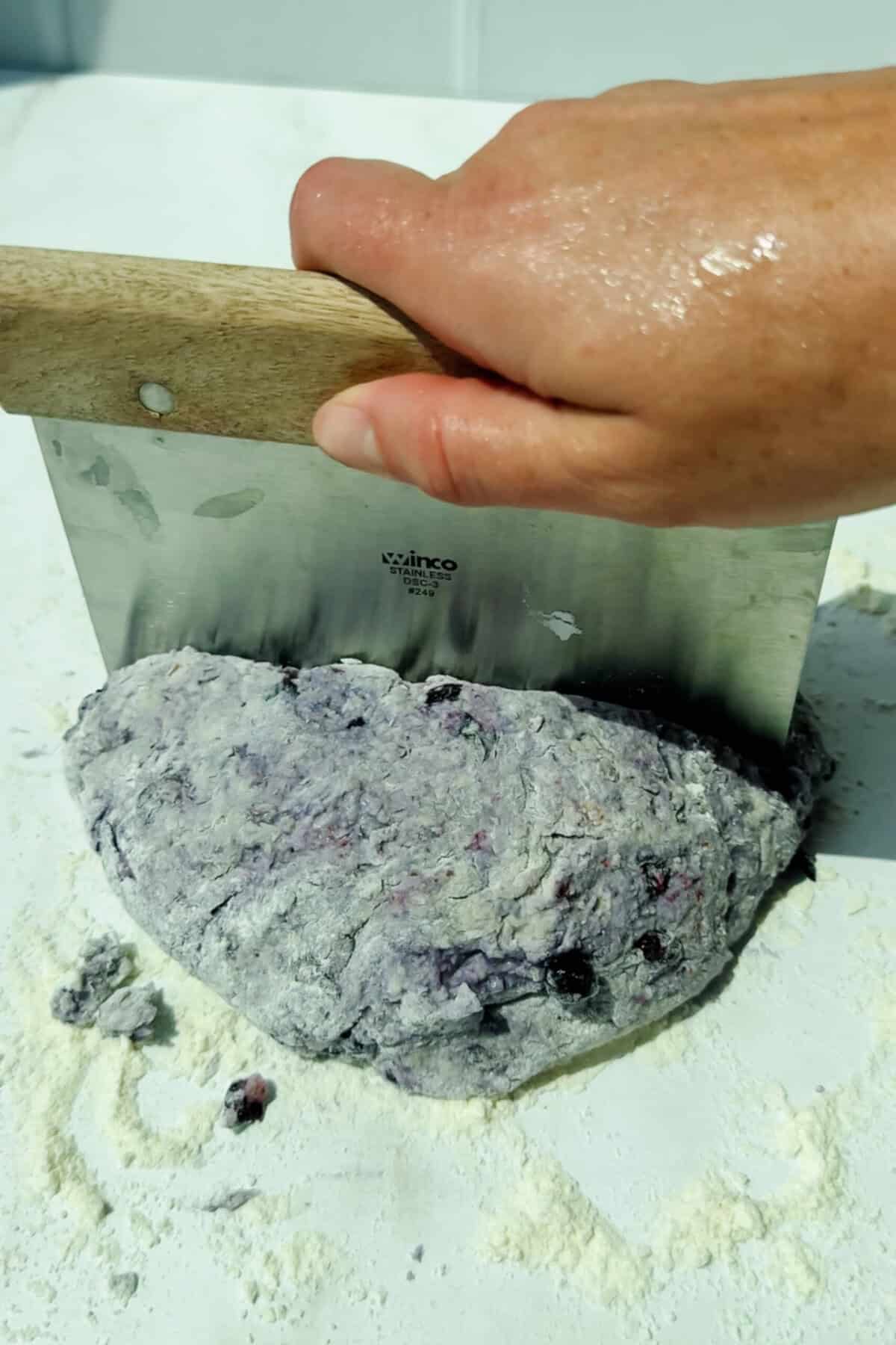 cutting blueberry biscuit dough on a floured surface with a dough scraper