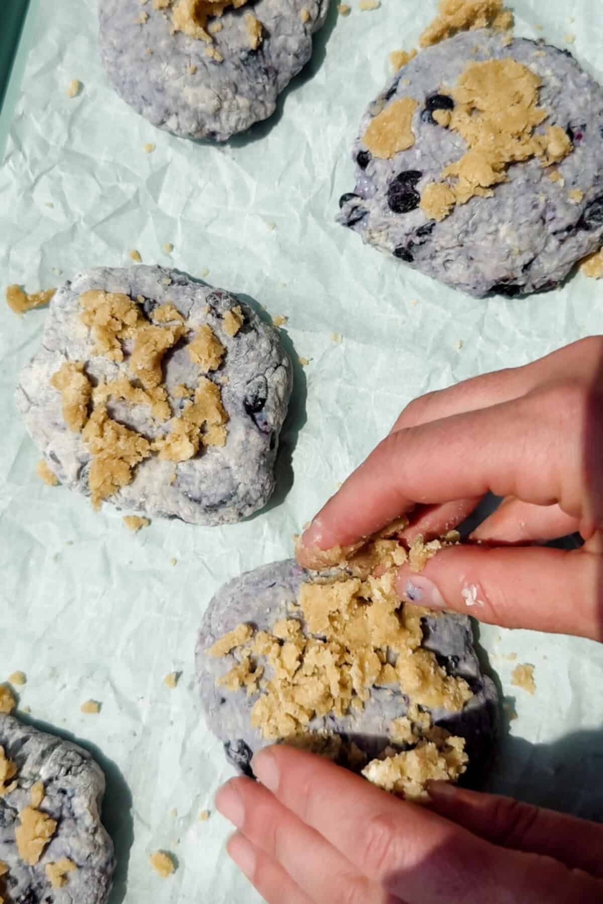 hand sprinkling streusel topping onto unbaked blueberry cottage cheese biscuits on parchment paper