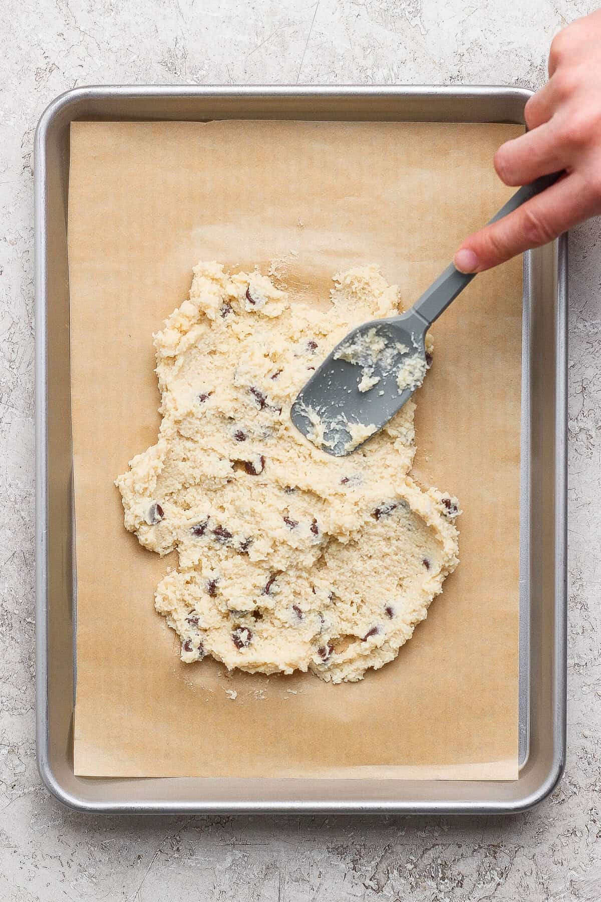 spreading cottage cheese cookie dough onto a parchment-lined baking sheet