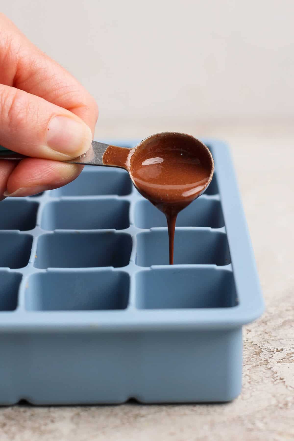 pouring melted peppermint chocolate over protein bite base in a silicone tray