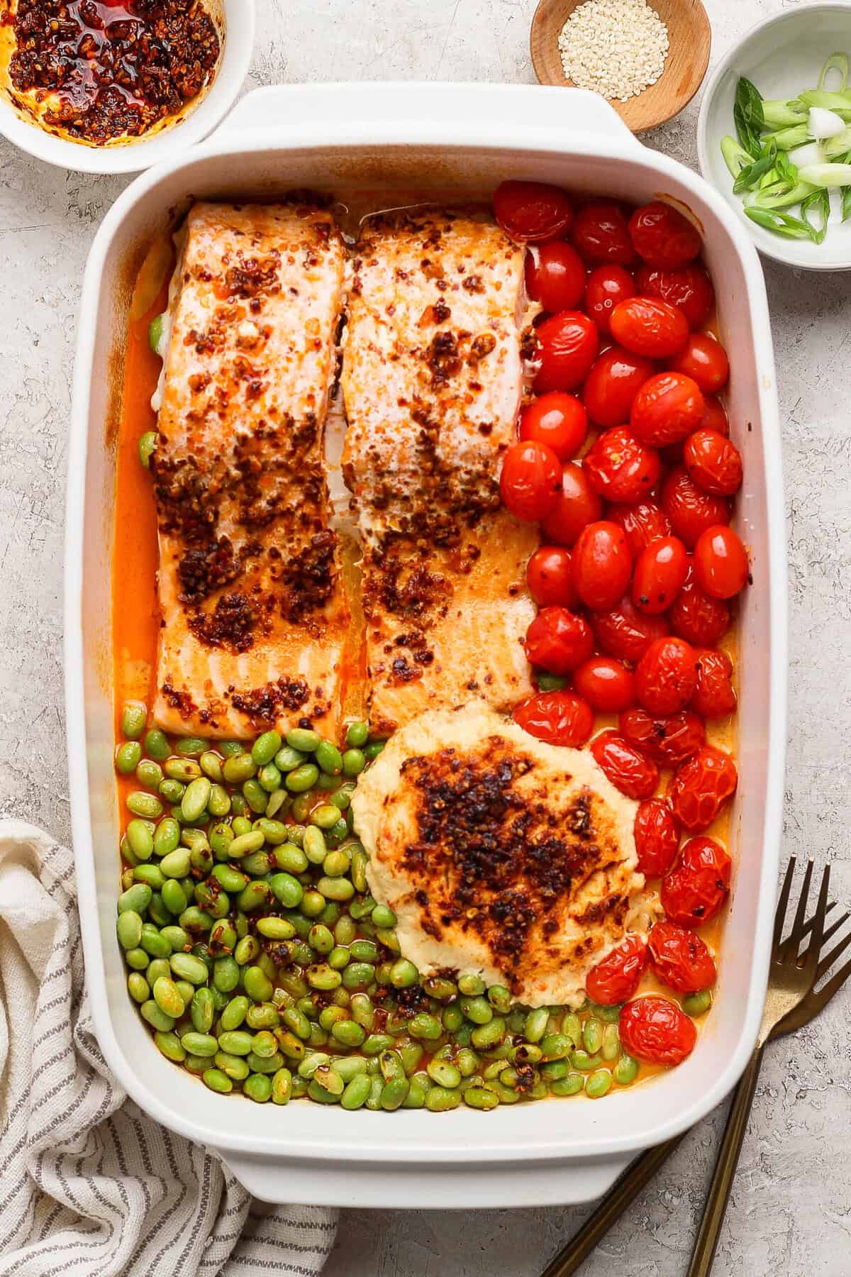 Close-up of baked chili crunch salmon with burst cherry tomatoes and edamame in a casserole dish