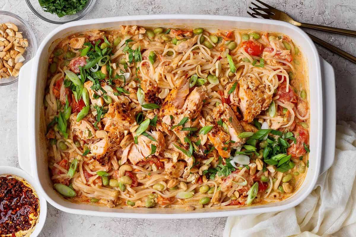 Salmon casserole with rice noodles, baked salmon chunks, cashews, green onions, cilantro, and chili crunch Boursin sauce in a white baking dish