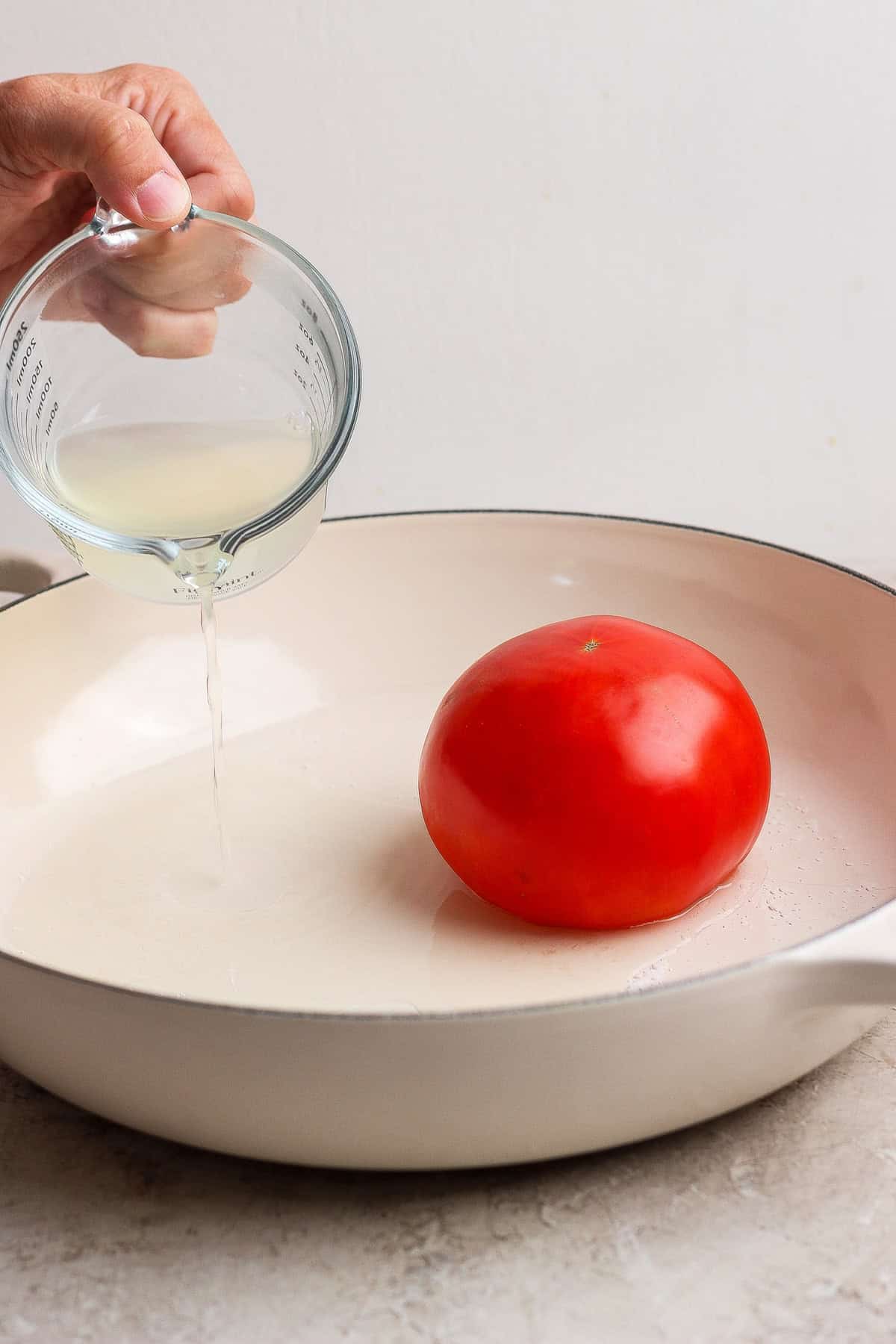 Reserved pasta water poured around a whole tomato in a skillet for steaming.