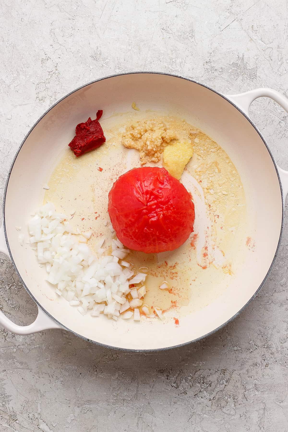 A peeled steamed tomato with diced onion, garlic, and tomato paste in a skillet.