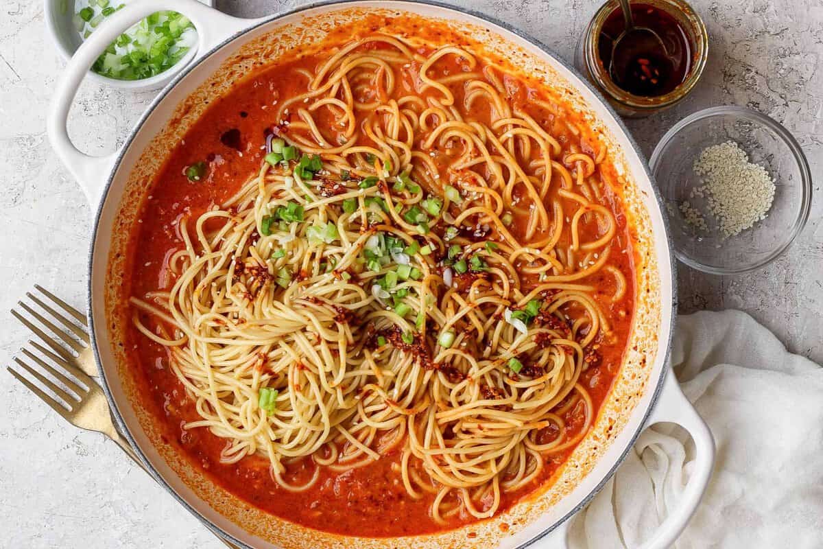 Chili crunch pasta served with green onions, sesame seeds, and extra chili crunch.