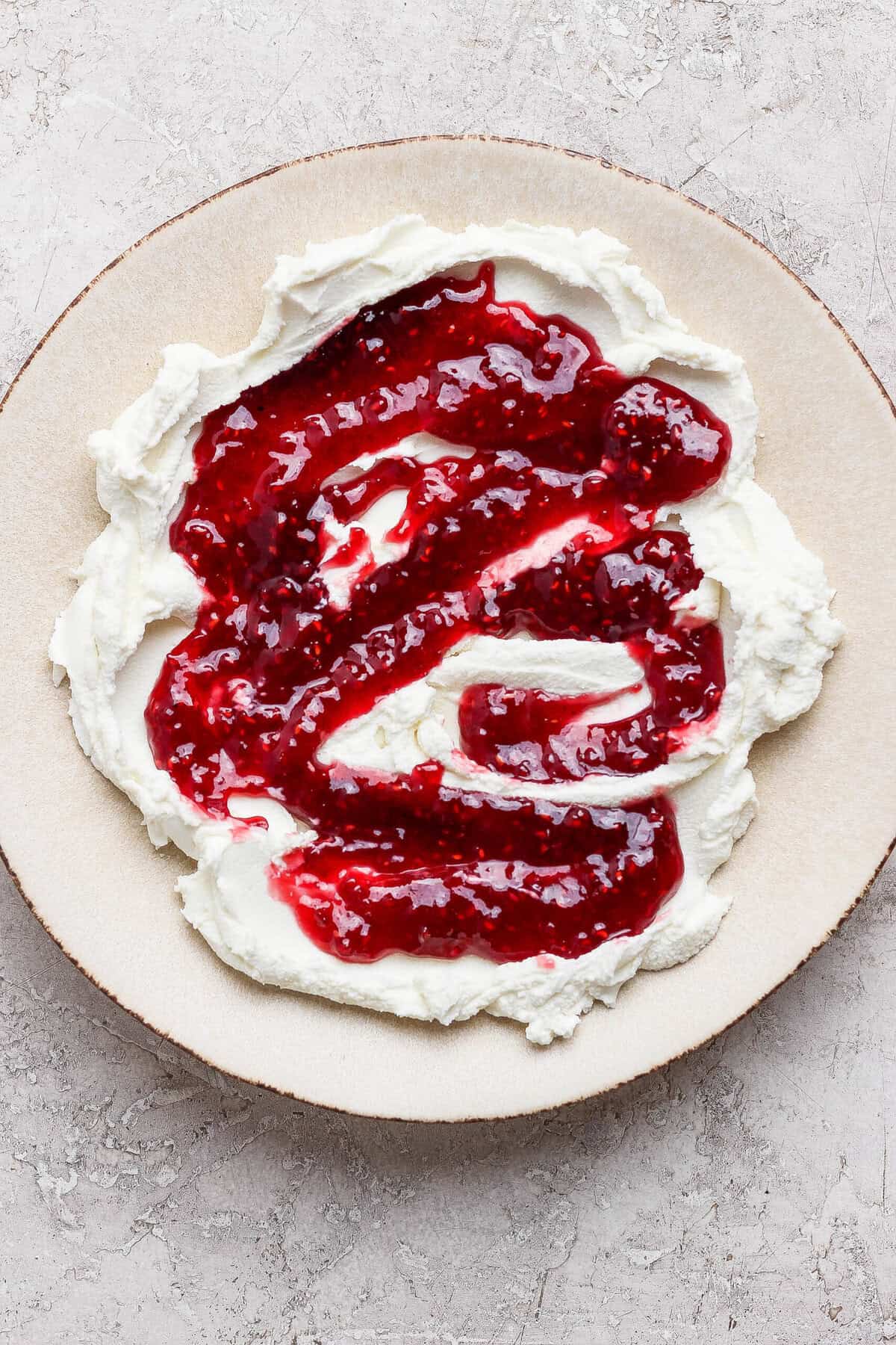 raspberry jam swirled over spread goat cheese on a plate