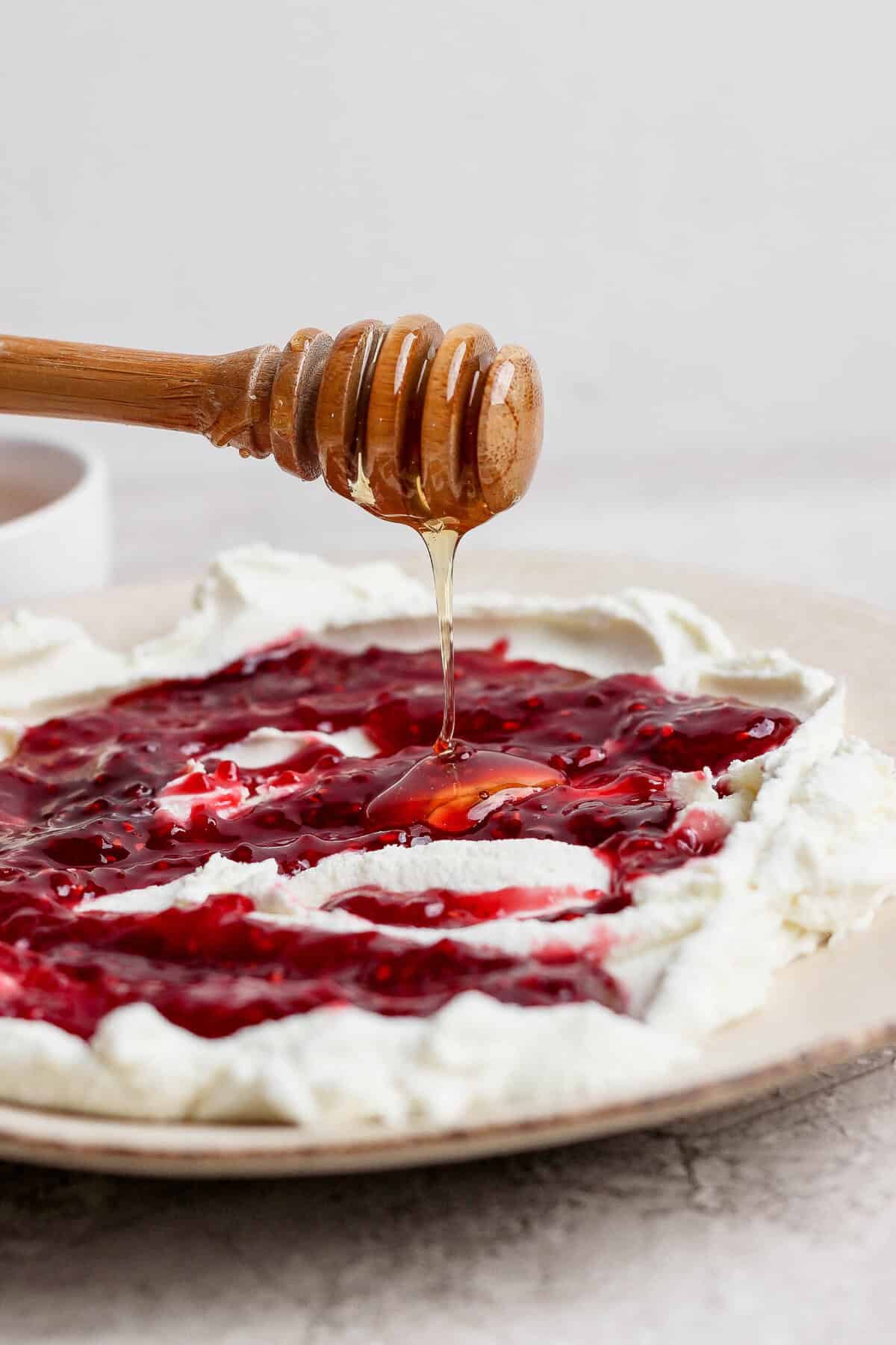 honey dipper drizzling hot honey over goat cheese dip with raspberry jam