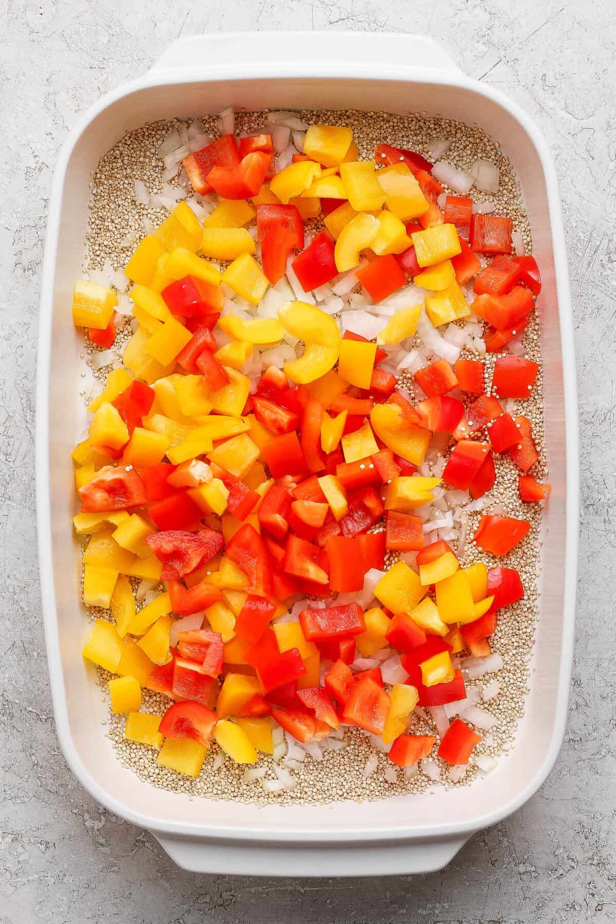 Uncooked quinoa, chopped bell peppers, and diced onion in a casserole dish for cashew chicken casserole.