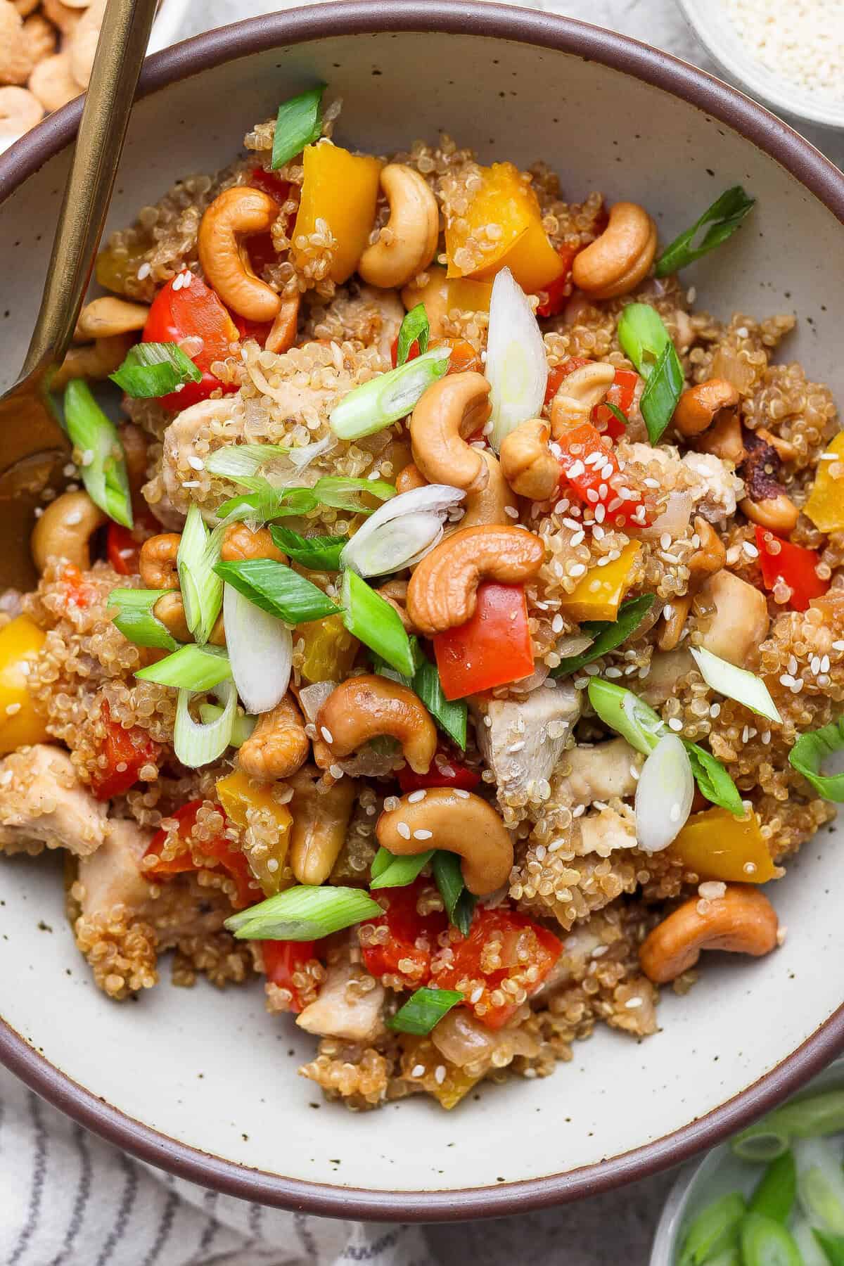 Serving of cashew chicken casserole with quinoa, bell peppers, and cashews in a bowl with a fork.