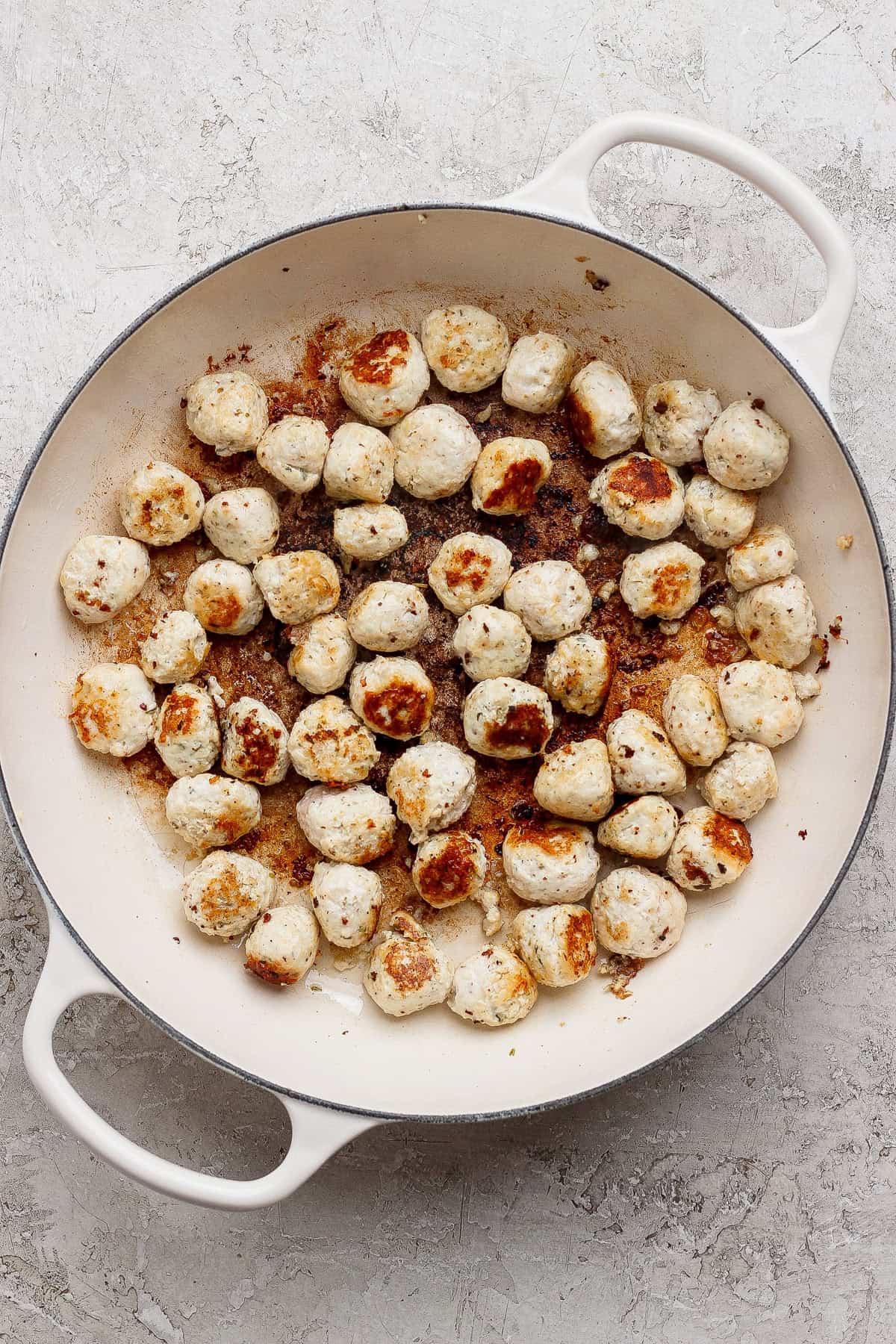 Browned mini chicken meatballs in a white skillet.