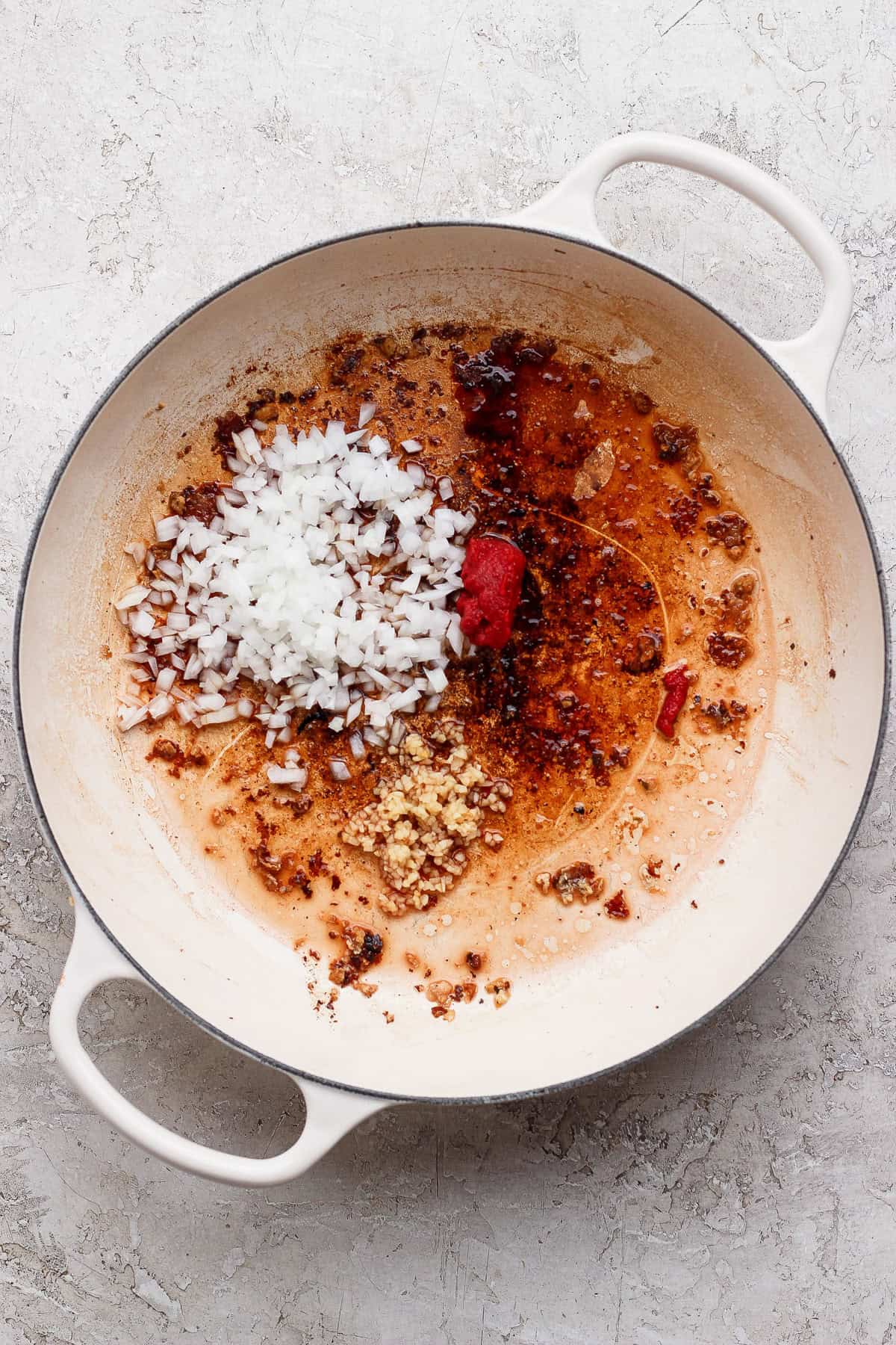 Minced onion, garlic, and tomato paste cooking in a white skillet for mini meatball pasta.