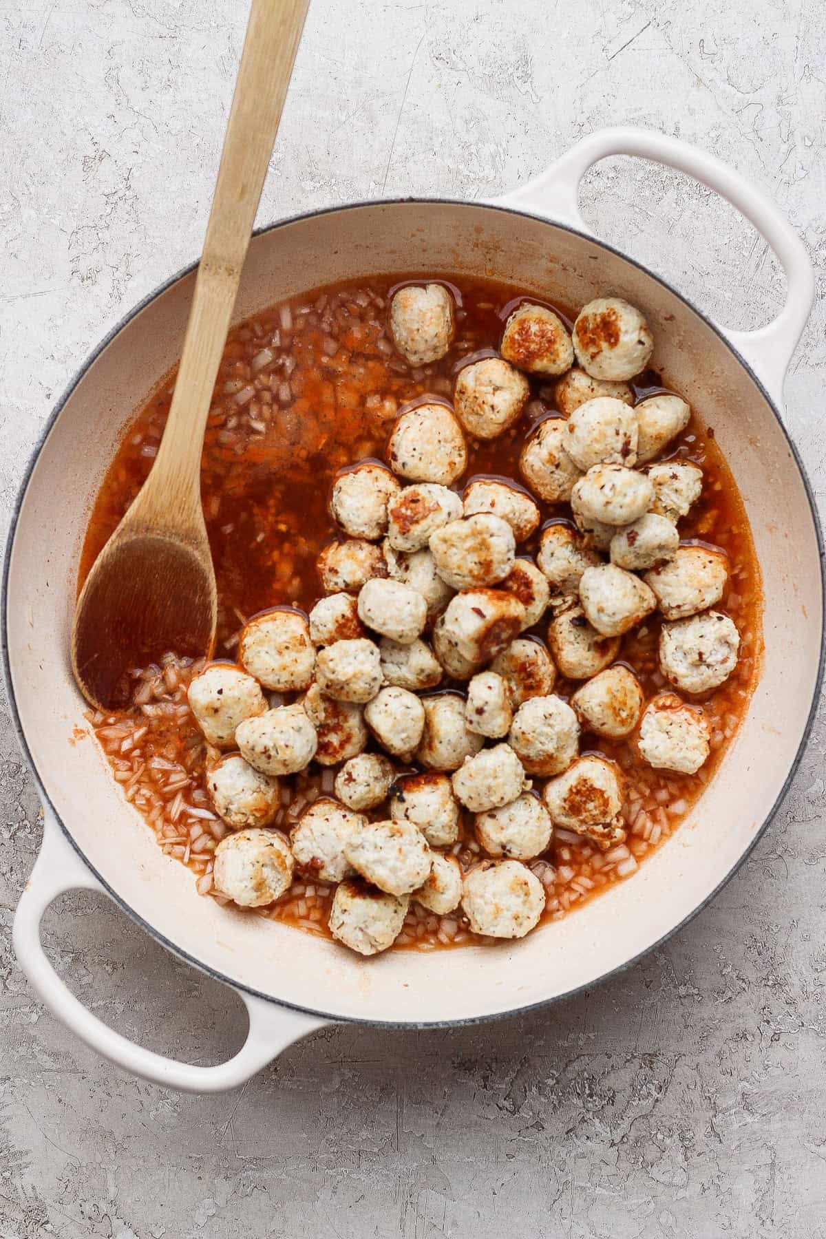 Mini chicken meatballs simmering in a light tomato pan sauce in a white skillet.