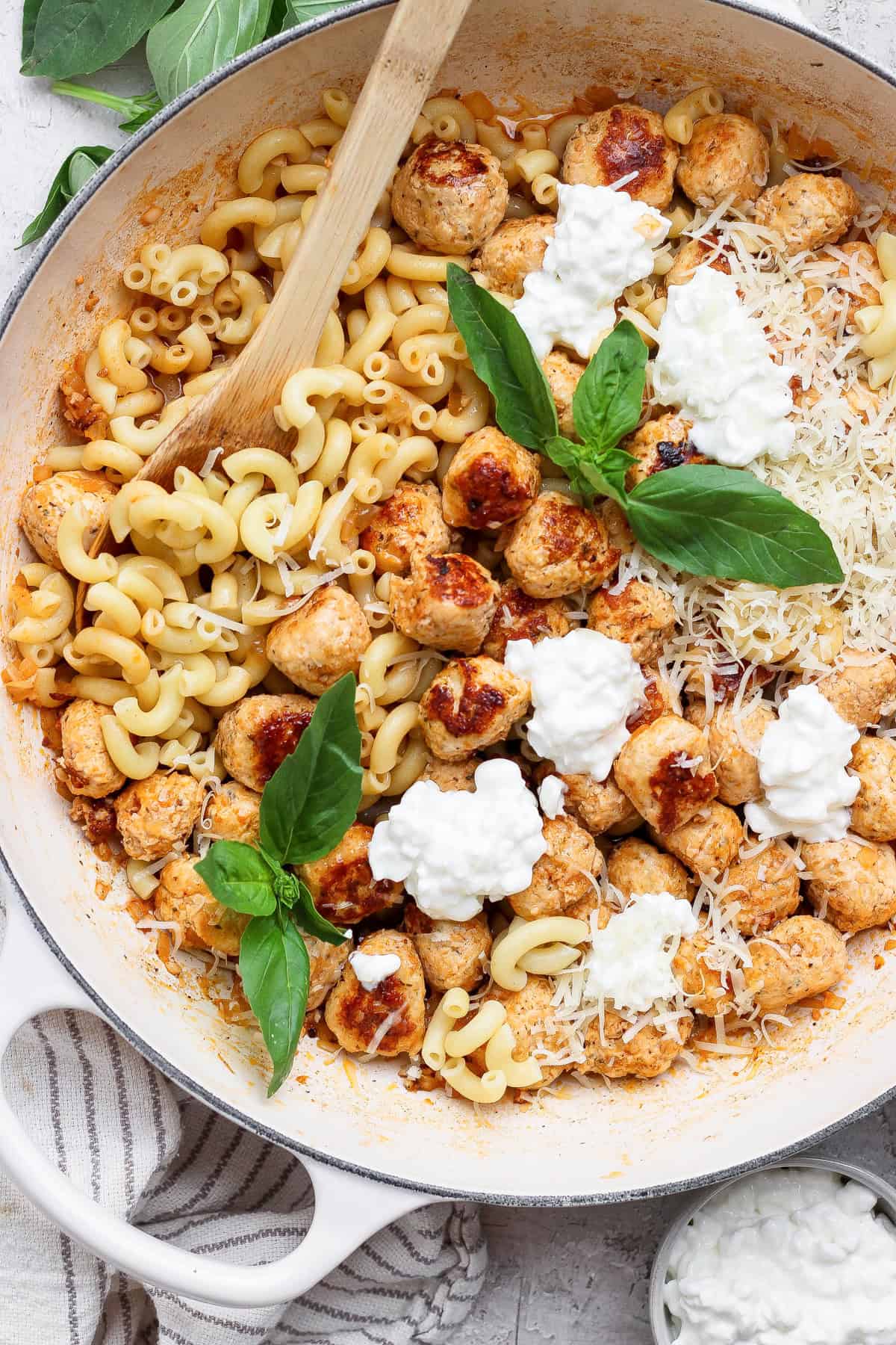Overhead view of mini chicken meatball pasta topped with cottage cheese, Parmesan, and fresh basil.