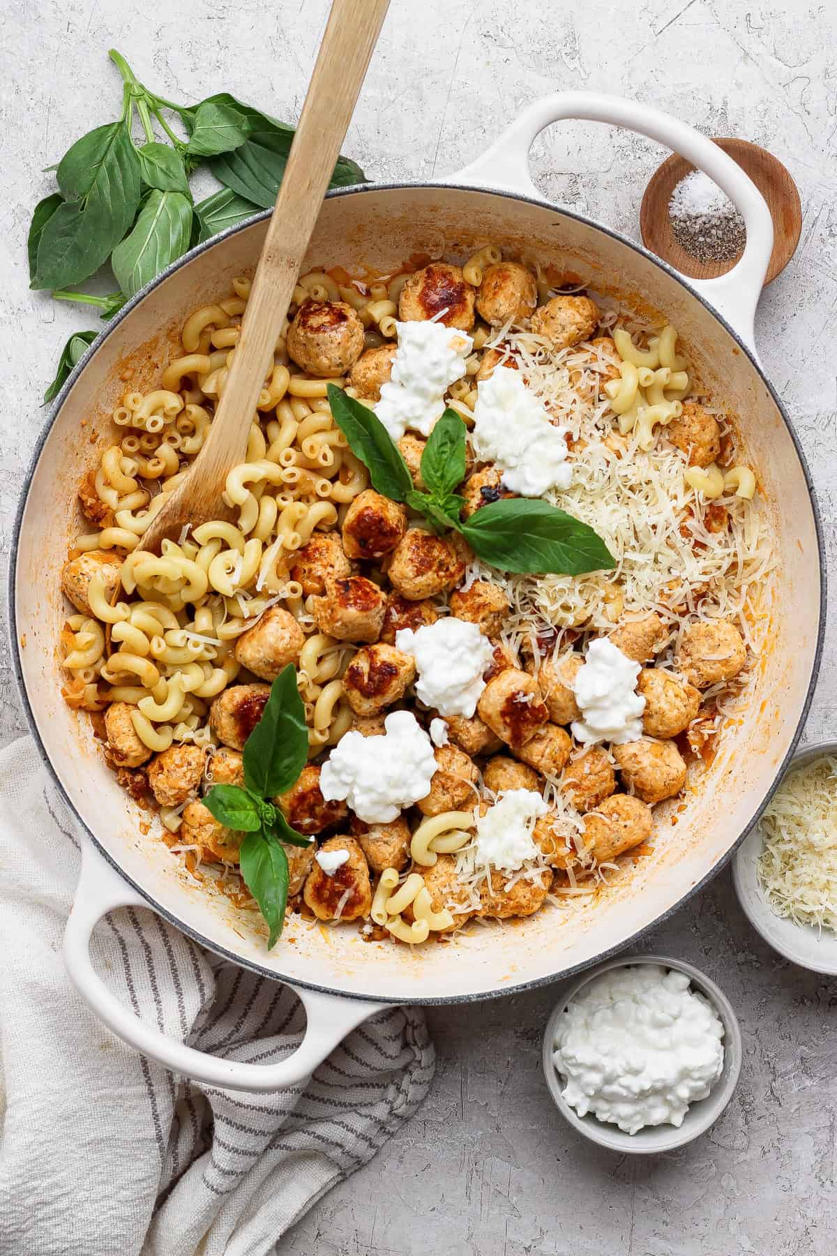 Finished mini cottage cheese meatball pasta in a white skillet with a wooden spoon.