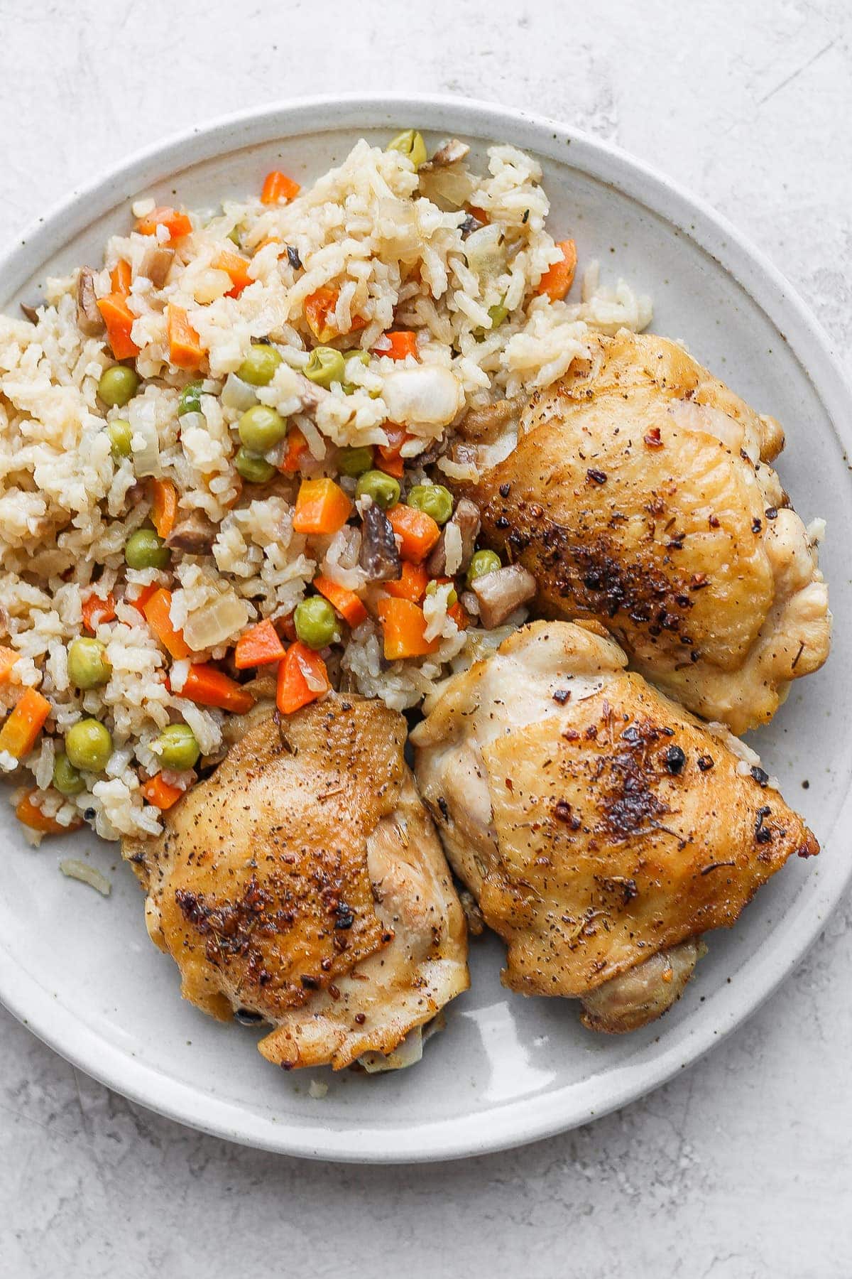 The most flavorful chicken and rice recipe on the internet. Our chicken and rice bake is made with juicy chicken thighs and a delightful rice medley so you get extra veggies! seared chicken thighs and rice on plate.