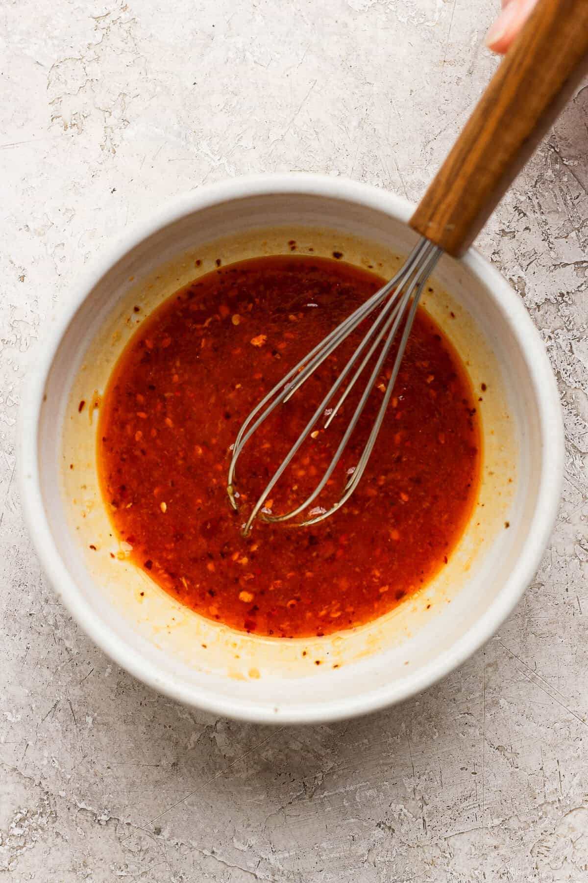 whisking chili crunch dressing with sesame oil ginger and lime in a ceramic bowl