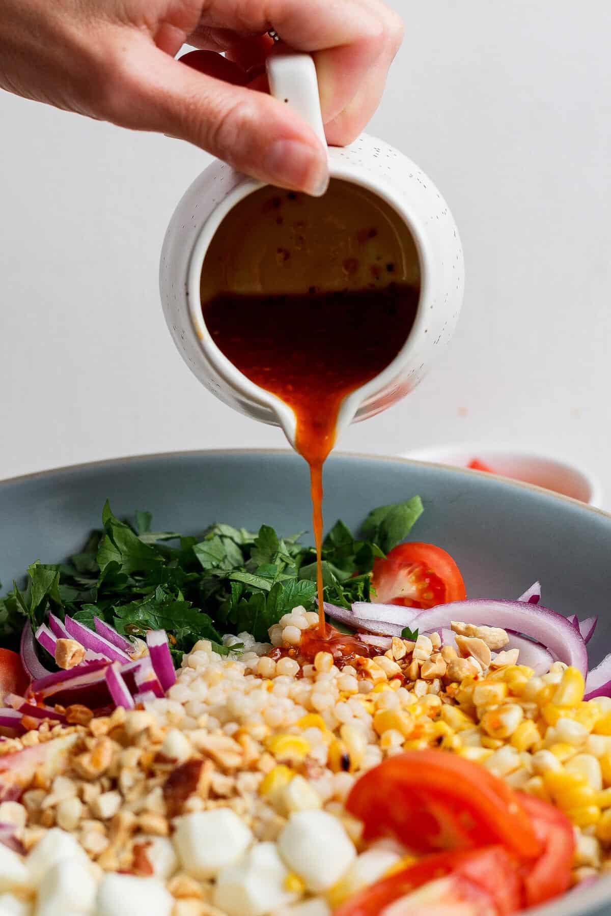 pouring chili crunch dressing over corn tomato salad from a pitcher