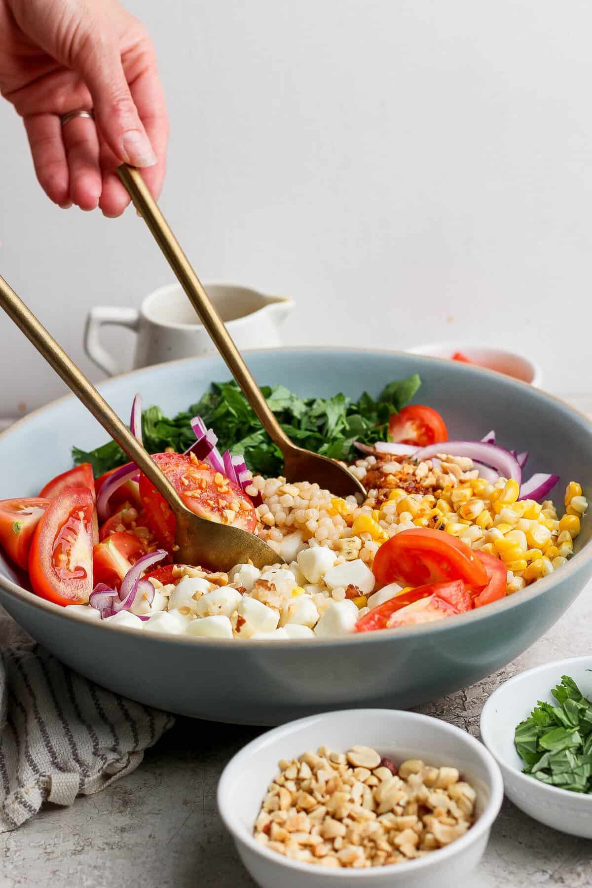 tossing corn tomato salad with chili crunch dressing in a large bowl