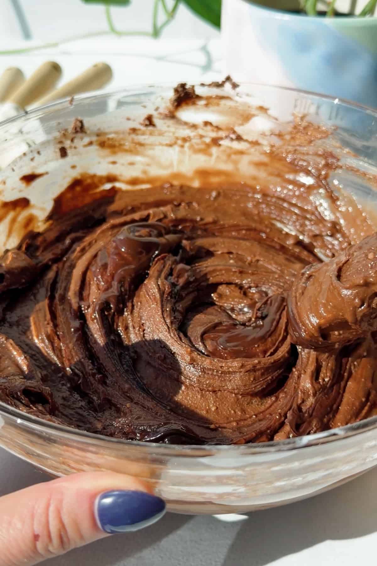 Thick chocolate brownie batter made with blended cottage cheese being stirred in a glass mixing bowl.