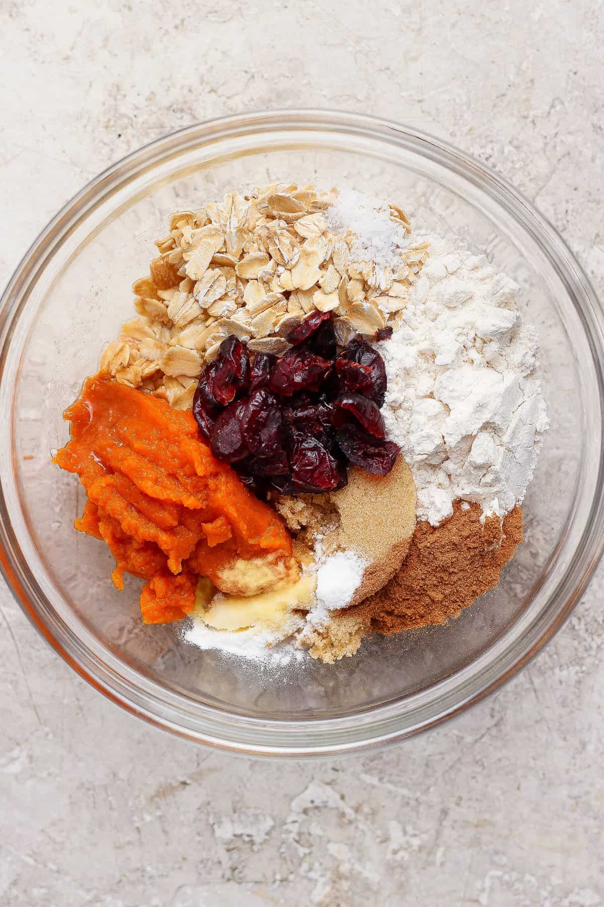 Oats, flour, brown sugar, pumpkin puree, dried cranberries, and spices in a glass mixing bowl.