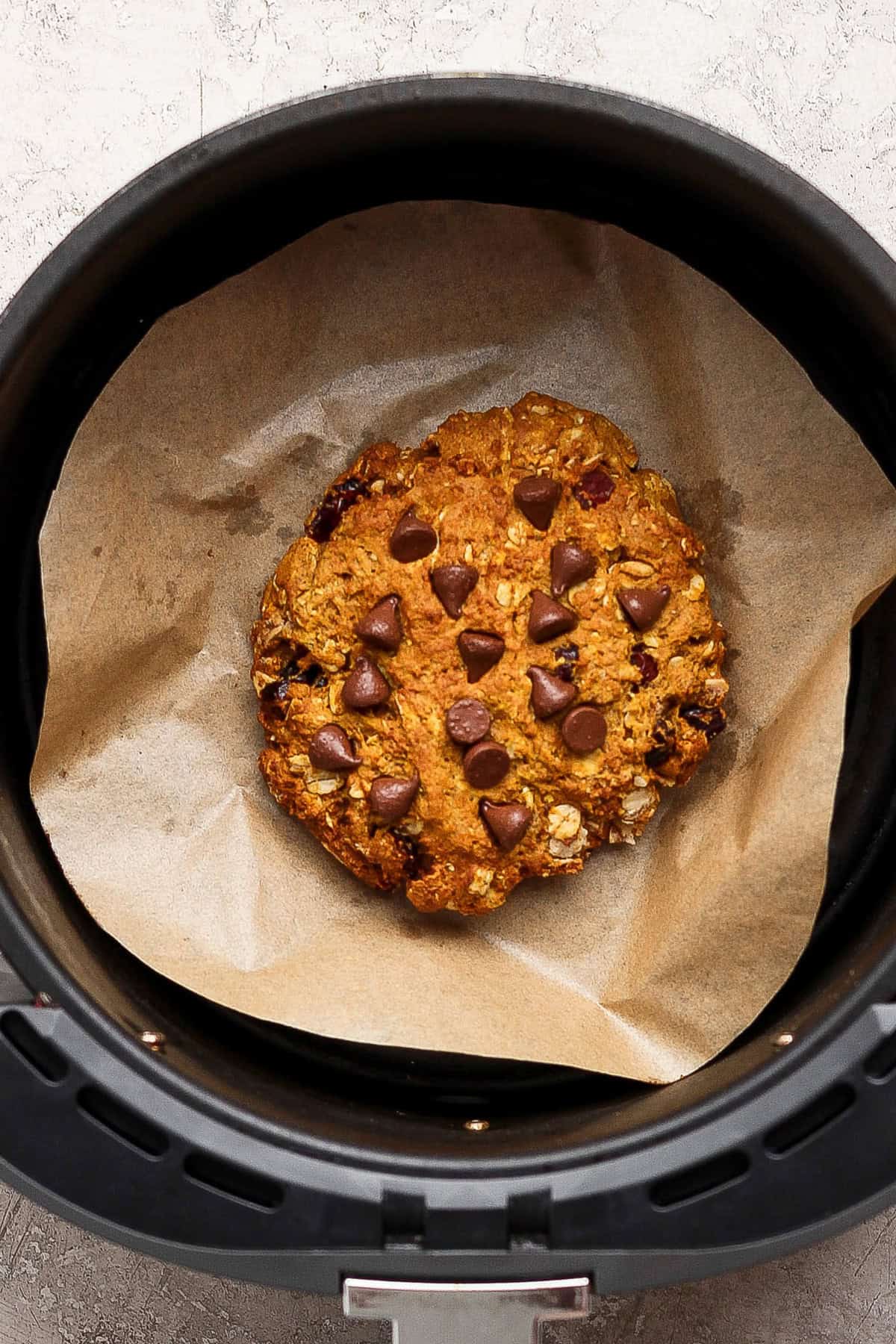 One pumpkin chocolate chip cookie on parchment inside an air fryer basket.
