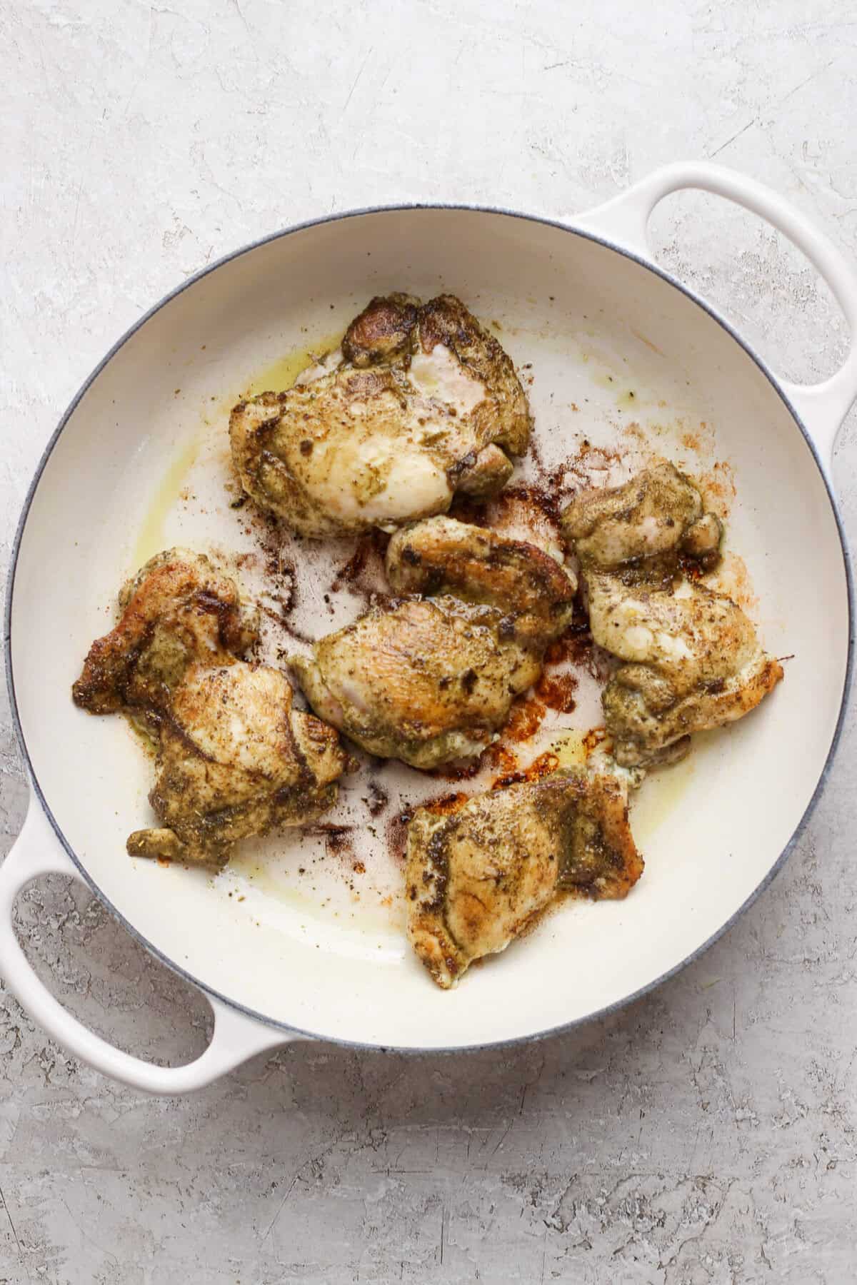 Chicken thighs seared until golden brown in a white skillet.