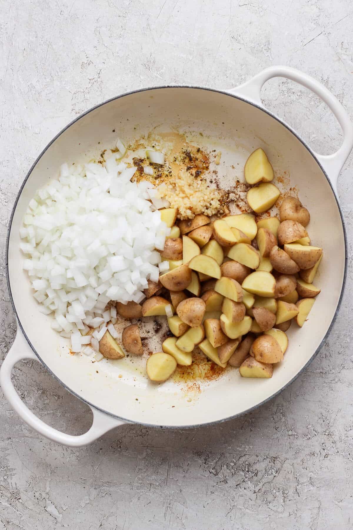 Diced white onion, minced garlic, and quartered baby potatoes in a white skillet.