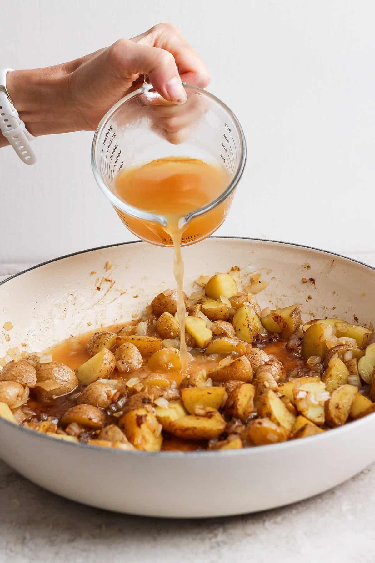 Apple cider being poured into a skillet of browned baby potatoes, onion, and garlic.