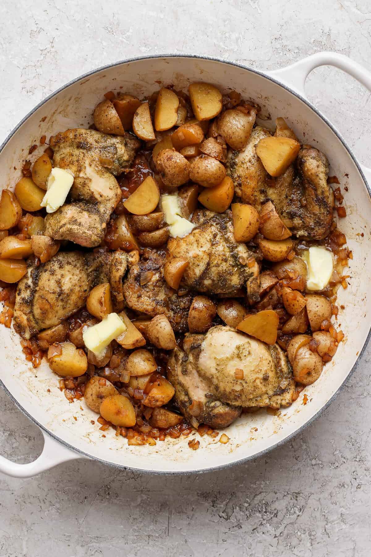 Butter melting into the apple cider pan sauce around chicken thighs, potatoes, and onion.