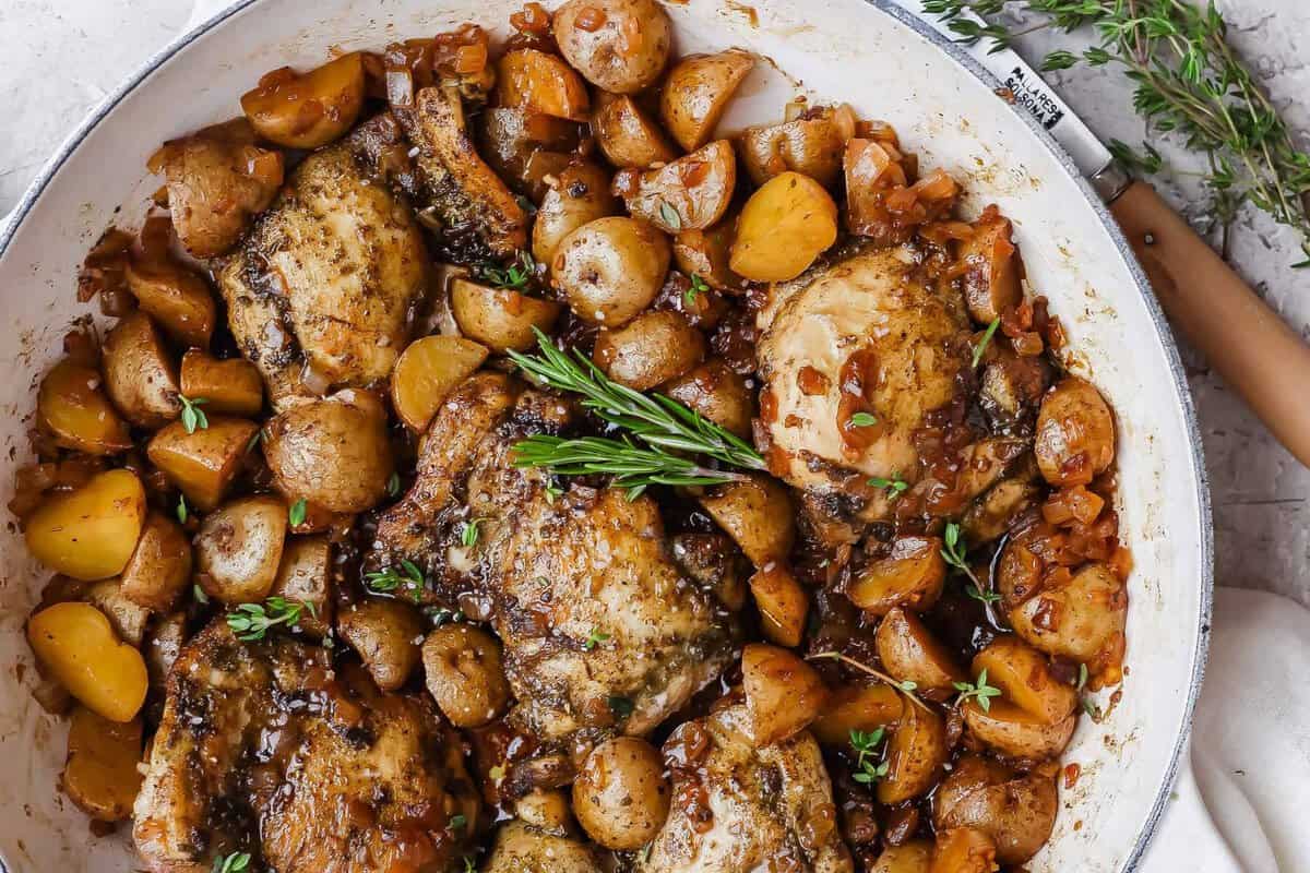 Apple cider chicken thighs nestled with baby potatoes and onion in a glossy skillet sauce.
